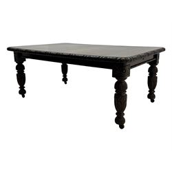 19th century heavily carved oak extending dining table, rectangular top with rounded corners and carved gadrooned edge, extending via winding mechanism with two additional leaves, raised on acanthus leaf-carved baluster supports terminating in ceramic castors