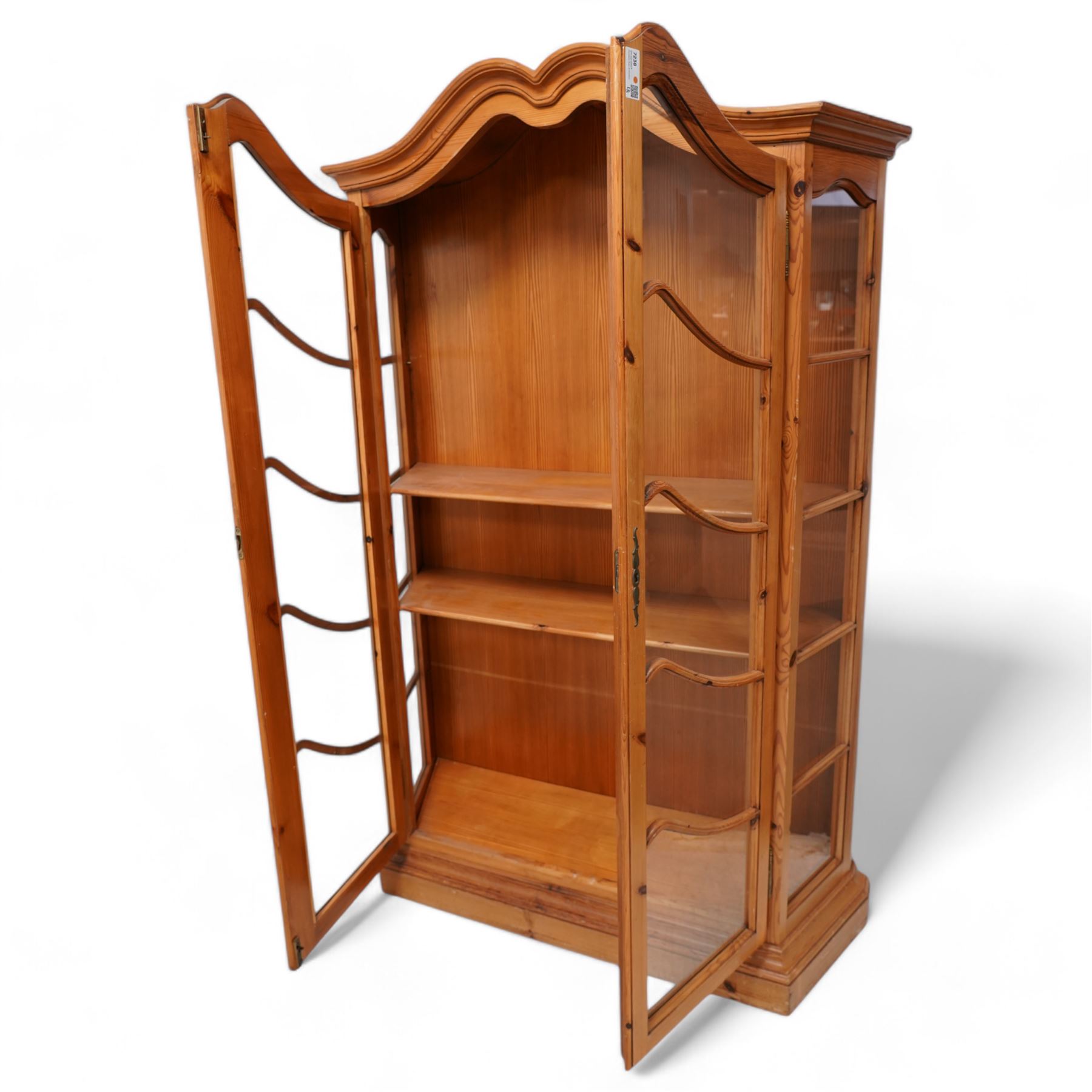 Polished pine display cabinet, shaped top over two glazed doors, fitted with three shelves, on moulded plinth base 