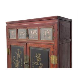 Late 19th century Chinese Qing dynasty red and black lacquered wood cabinet, Fujianese province, upper cupboard enclosed by two doors with relief carved and gilt panels depicting figures behind glass, the large cupboard enclosed by two panelled doors carved with trailing foliate branches and birds, inscribed with Chinese characters, to the left ‘Prolong life’ and to the right ‘Wealth and good fortune’, fitted with two drawers, square supports with carved brackets 