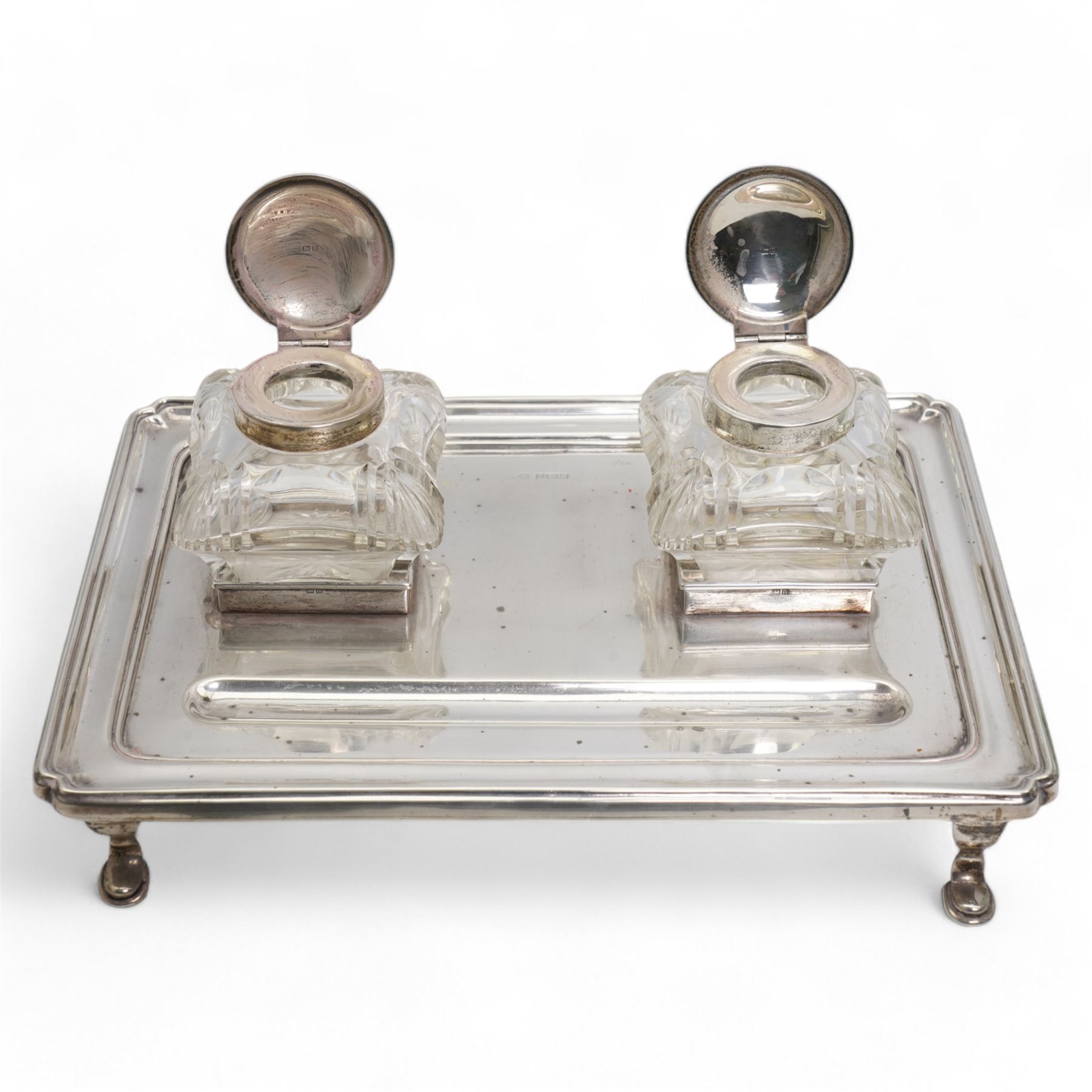 George V silver inkstand of rectangular design with pen tray and two cushion shape glass inkwells with silver covers, raised edge and four shaped supports 28cm x 20cm Birmingham 1912 Maker William Hutton & Sons