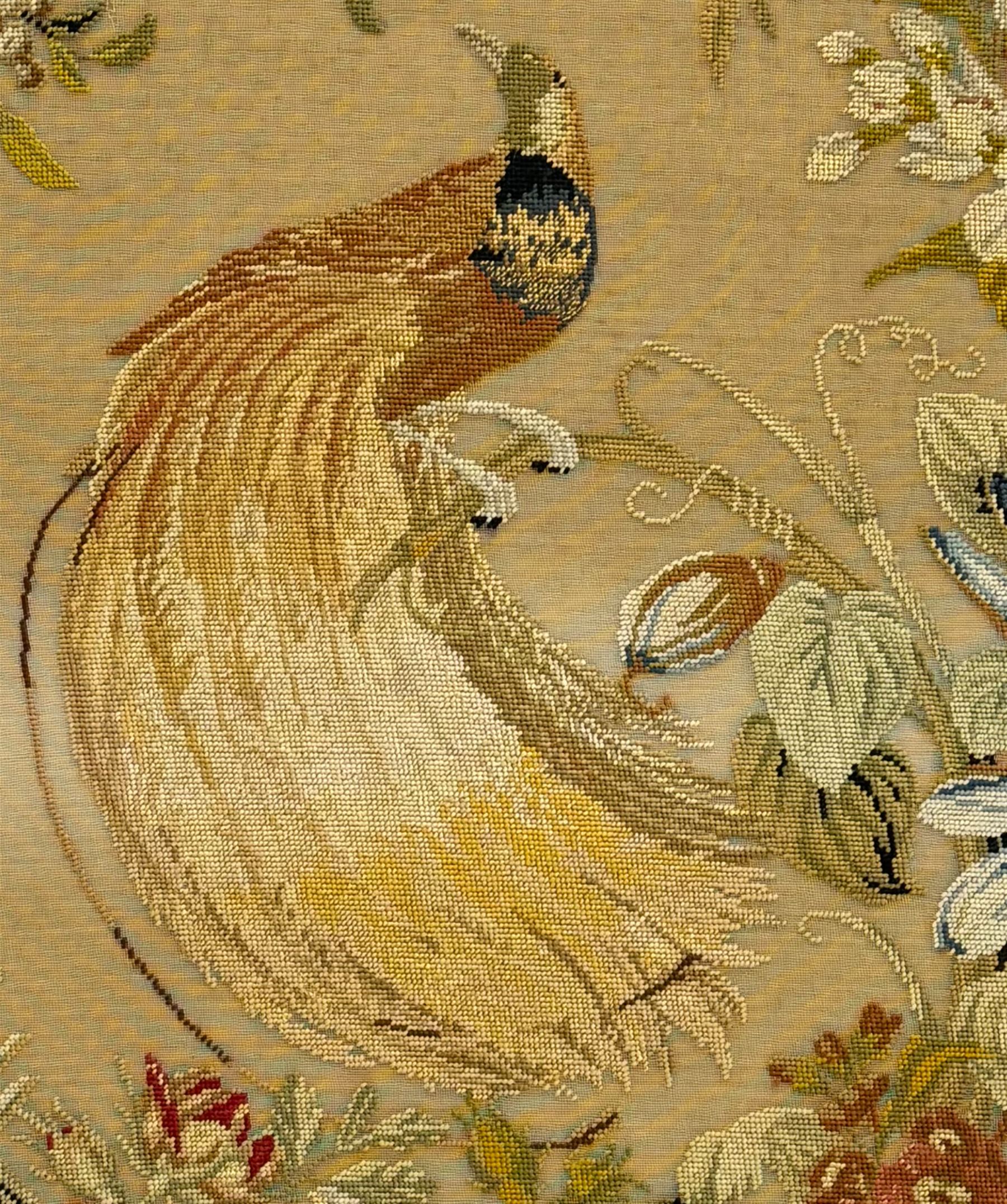 Early 20th century walnut carved needlepoint wall panel, depicting peacock amongst a floral arrangement, framed by carved border with scrolled crest and acanthus leaf accents