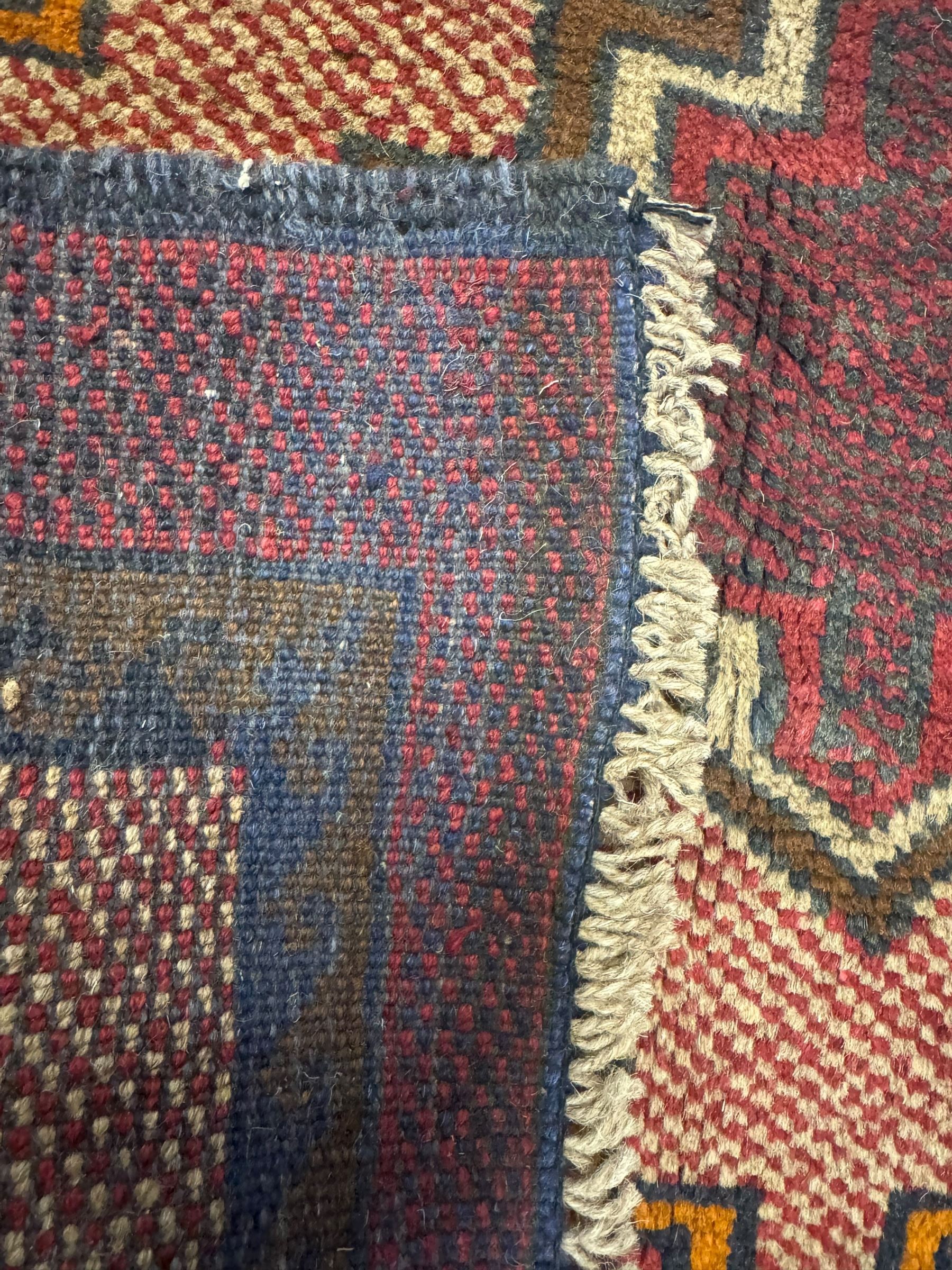 Baluchi crimson ground rug, the central field decorated with two stacked geometric lozenge medallions, surrounded by stepped multicoloured motifs, the wide border with alternating angular motifs in deep red, within a narrow brown guard stripe