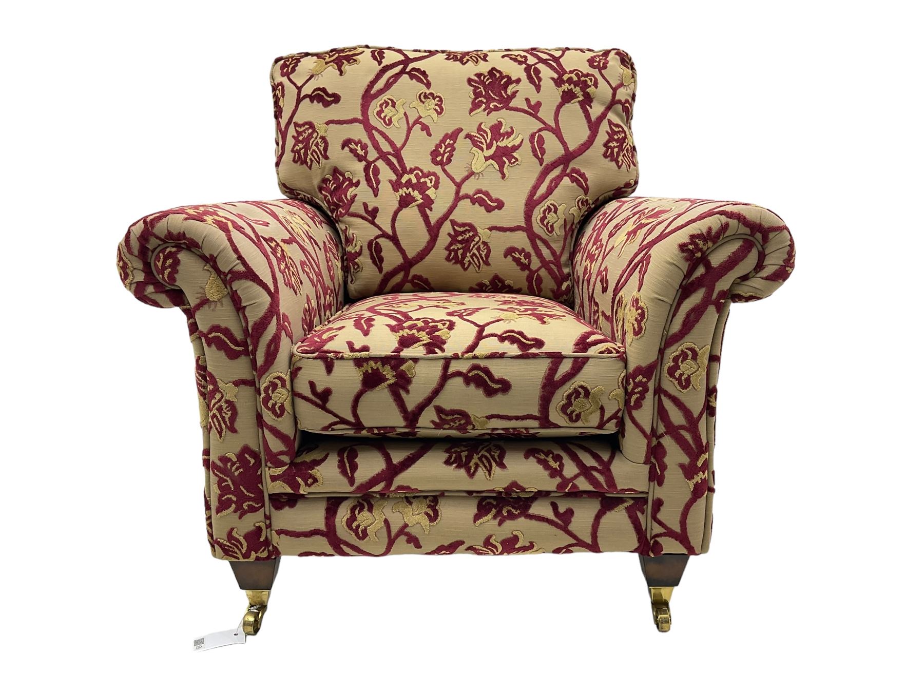 Contemporary upholstered armchair, scroll arms and loose cushions, embossed beige ground fabric with red and gold floral motifs, on tapered wooden supports with front brass castors