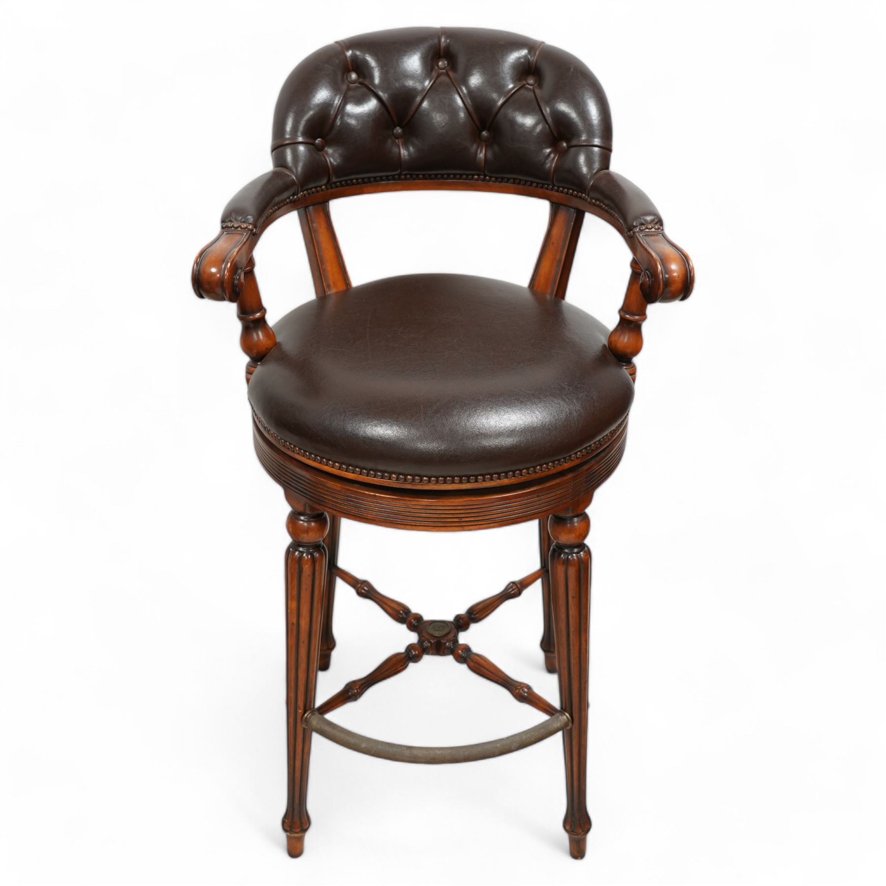 Pair of hardwood-framed bar stools, revolving tub seat with buttoned back rest and upholstered seat in brown leather, reed moulded seat rail over four lobe carved tapering supports, united by metal foot rest and x-framed stretchers 