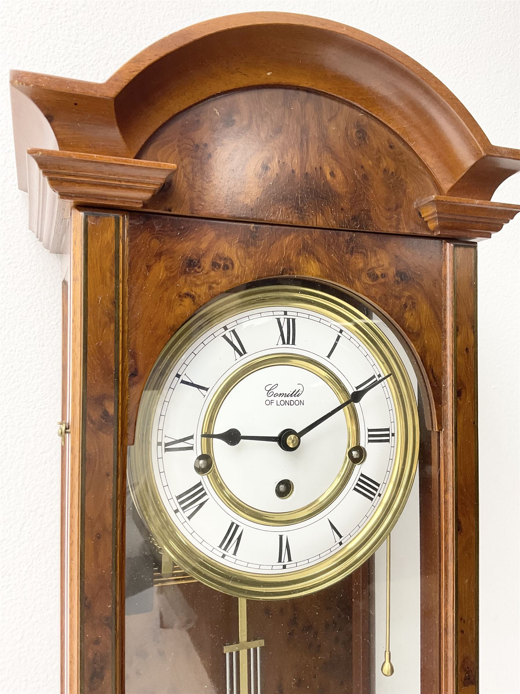 Comitti,  London - 20th century 8-day chiming wall clock in a walnut case, with a moulded break-arch top and full length glazed door and side panels, two part enamel dial with spade hands and visible gridiron pendulum, three train spring driven movement chiming the quarters on 5 gong rods.