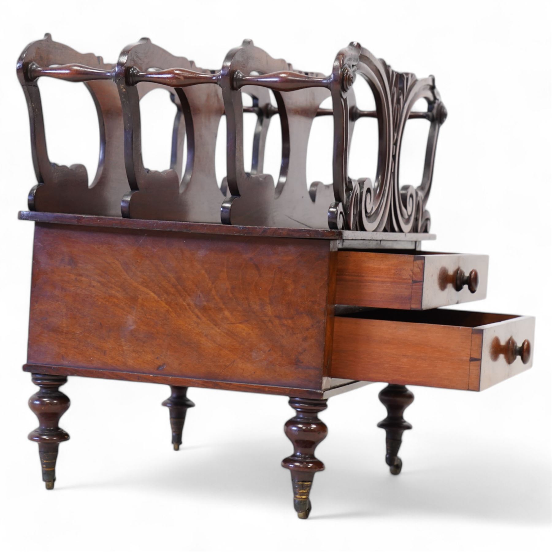 Victorian mahogany Canterbury, three divisions, carved with scrolls and curled leaf motifs, fitted with two drawers, on turned feet with brass cups and castors 