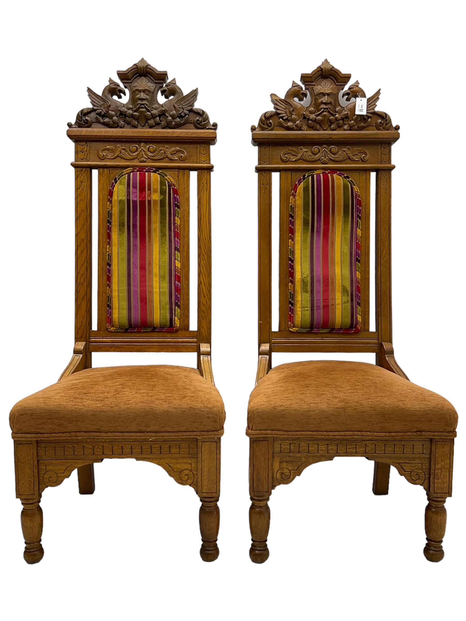 Set of six 20th century Carolean design oak high back chairs, the pediment carved with dragons and central Green Man mask with trailing foliage, the backs upholstered in striped fabric, on turned front supports