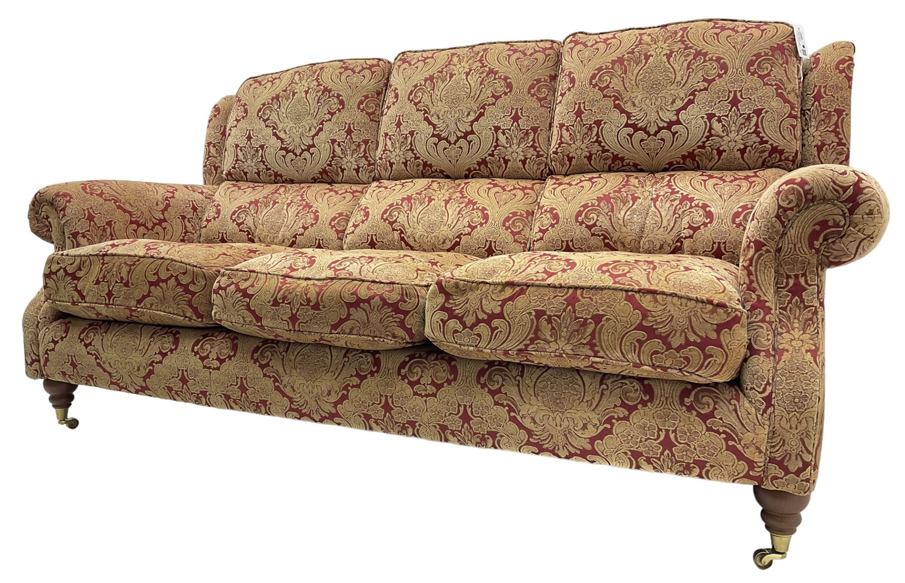 Parker Knoll - three-seat 'Oakham' hardwood-framed sofa, upholstered in red and gold floral pattern fabric, on turned feet with brass cups and castors 