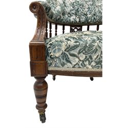 Victorian walnut framed tub-shaped armchair, the shaped rolled back supported by a spindle turned balustrade, upholstered in buttoned floral fabric, scrolled arms supports carved with acanthus leaves and flower heads, on collar turned feet with brass and ceramic castors