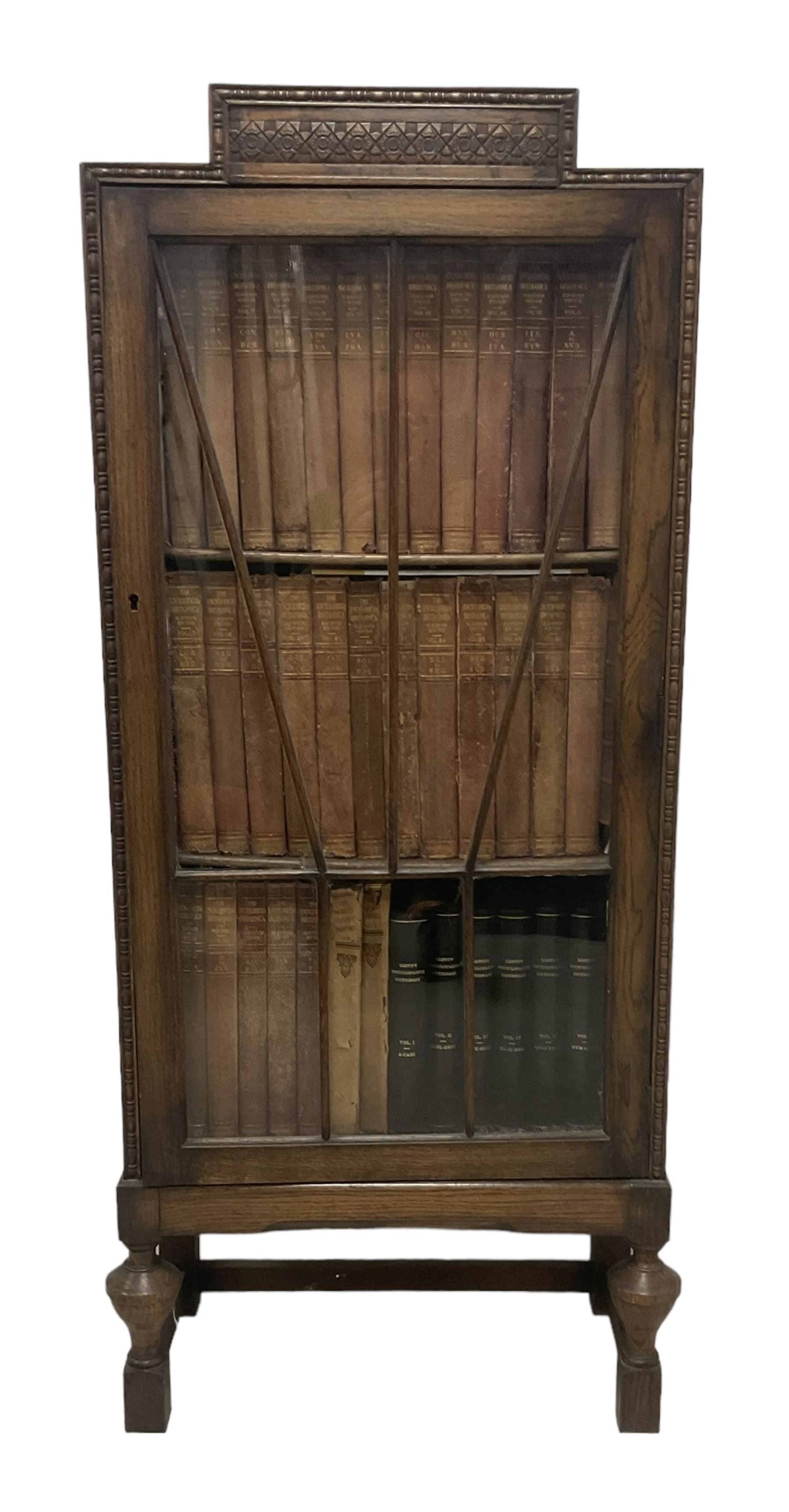 Edwardian oak bookcase, stepped top decorated with beading and stylised floral frieze, single astragal glazed door enclosing encyclopaedias and other books, on turned front feet united by plain stretchers 