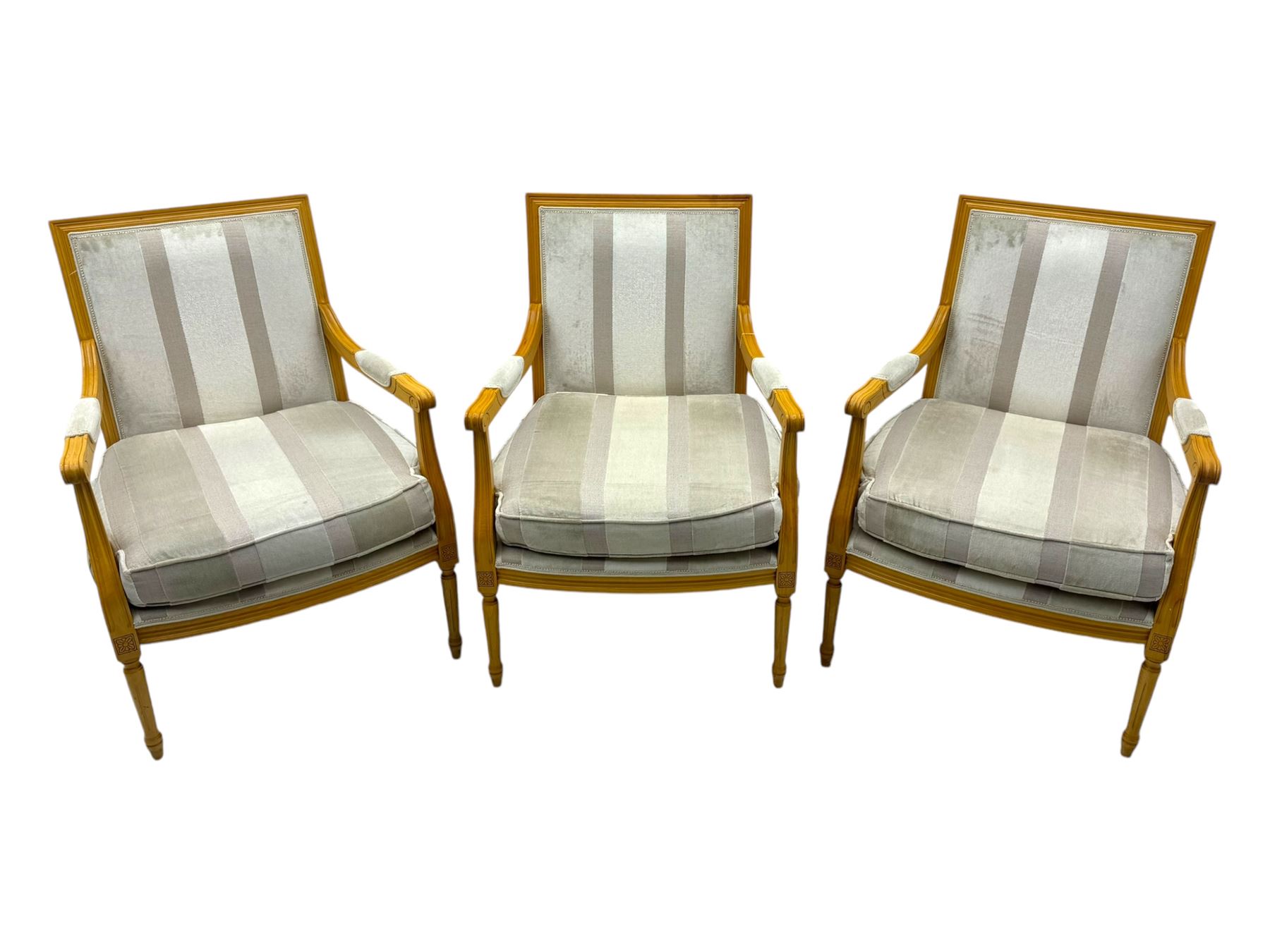 Three mid-20th century beechwood fauteuil armchairs, upholstered backrest and seat in cream stripe fabric, padded armrests with scroll detail, on tapered fluted supports with carved floral rosette blocks