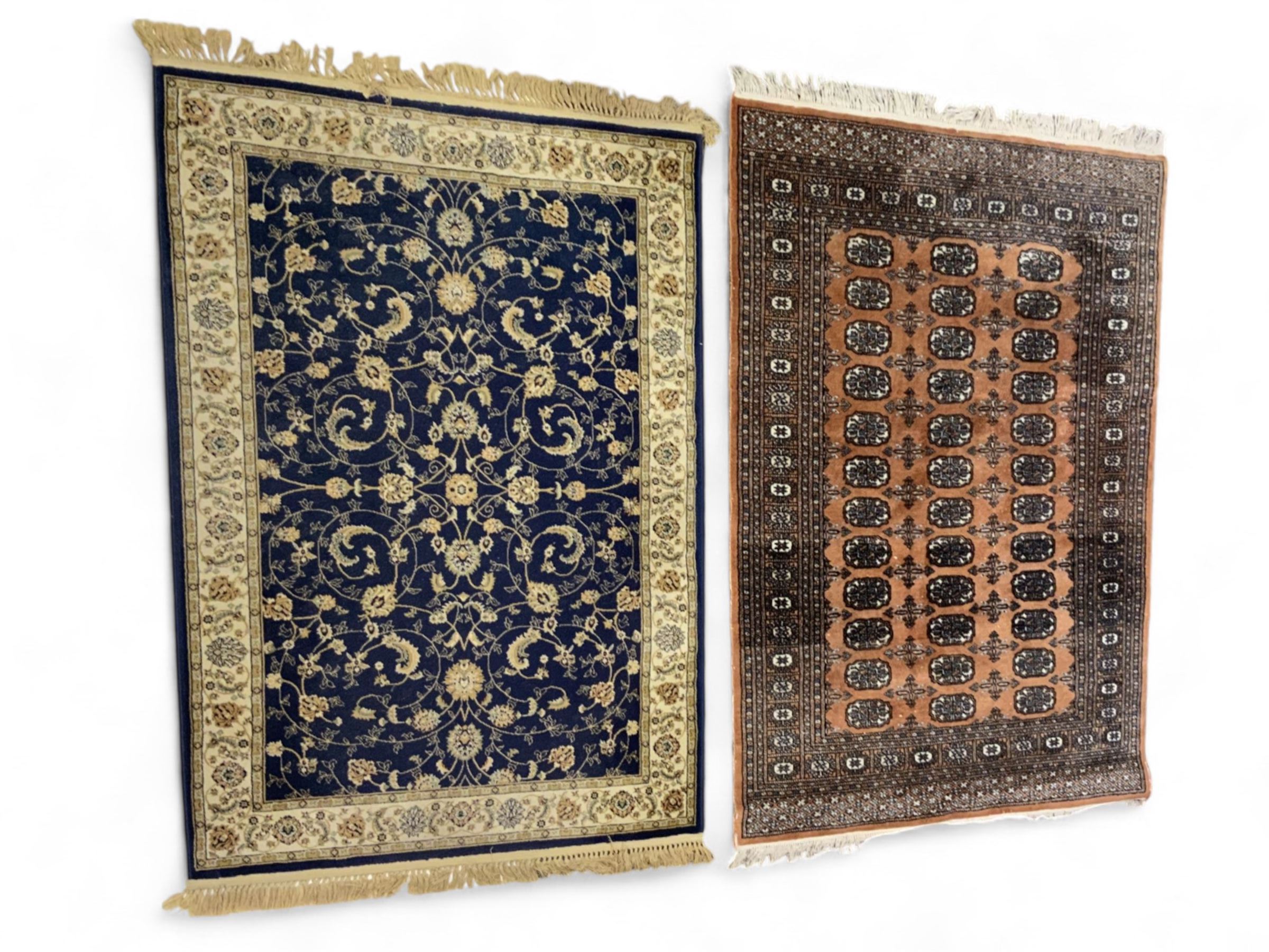 Afghan Bokhara rust ground rug, decorated with three columns of Gul motifs, the wide guard band with further scrolling and geometric designs (183cm x 129cm); together with a Persian design indigo ground rug (W170cm x 117cm)