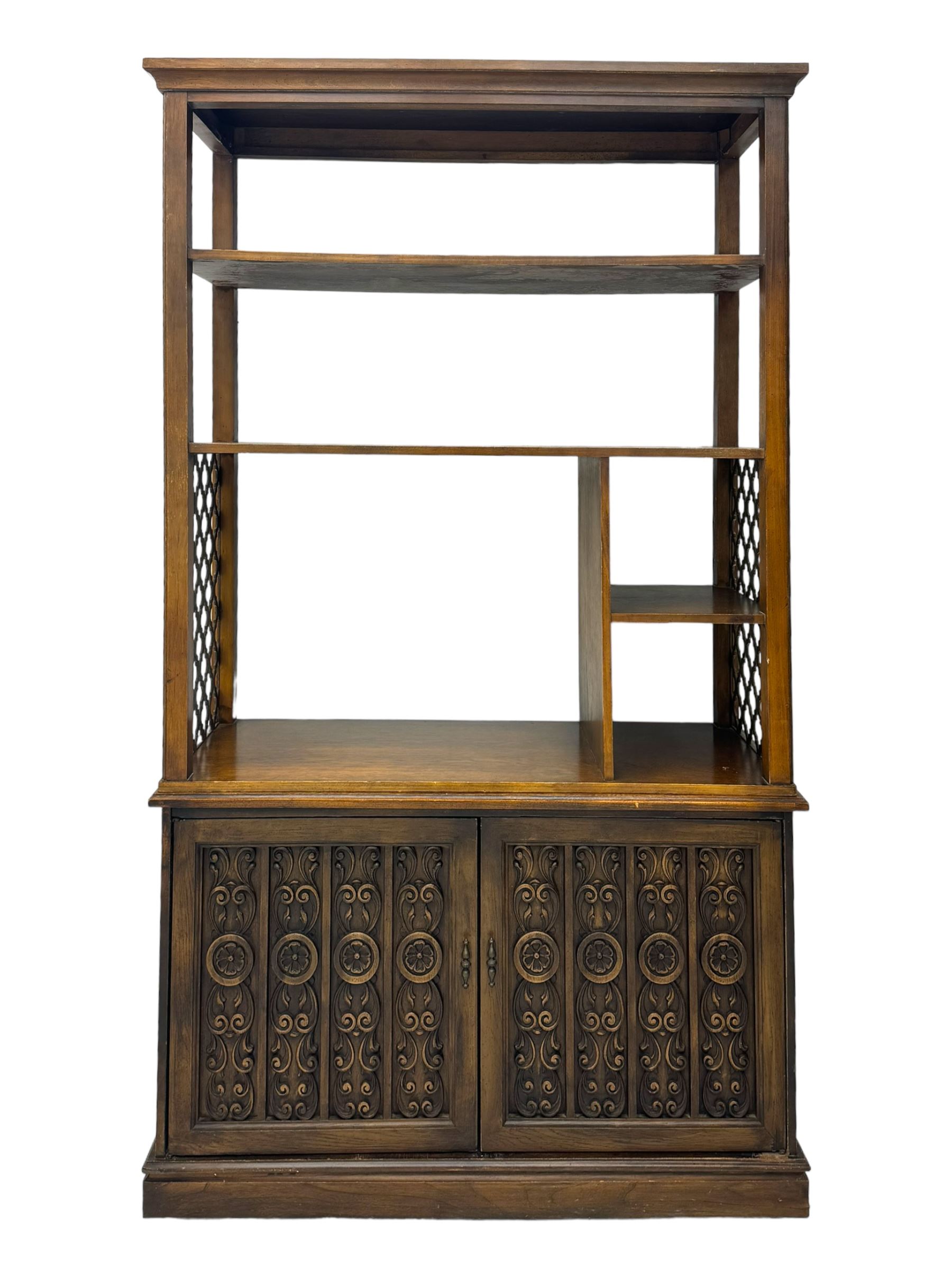 Mid 20th century oak bookcase cupboard, projecting cornice over three open shelves with subdivided sections and latticework uprights, two doors to the base with floral and scrollwork carvings and central brass handles, resting on a moulded plinth base