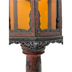 20th century Chinese black and red lacquered hardwood lantern stand, hexagonal shaped canopy top carved with flower heads and scrolls, the lantern fitted with amber tinted glass panes, pierced and carved upper panels, enclosed by two hinged doors, turned stem carved in relief with trailing vine leaves with fruits, stepped hexagonal base with carved decoration  