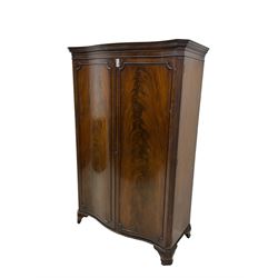 Early 20th century mahogany serpentine double wardrobe, moulded cornice over two figured doors, the interior fitted with hanging rail and shelf, canted and fluted uprights, on bracket feet 