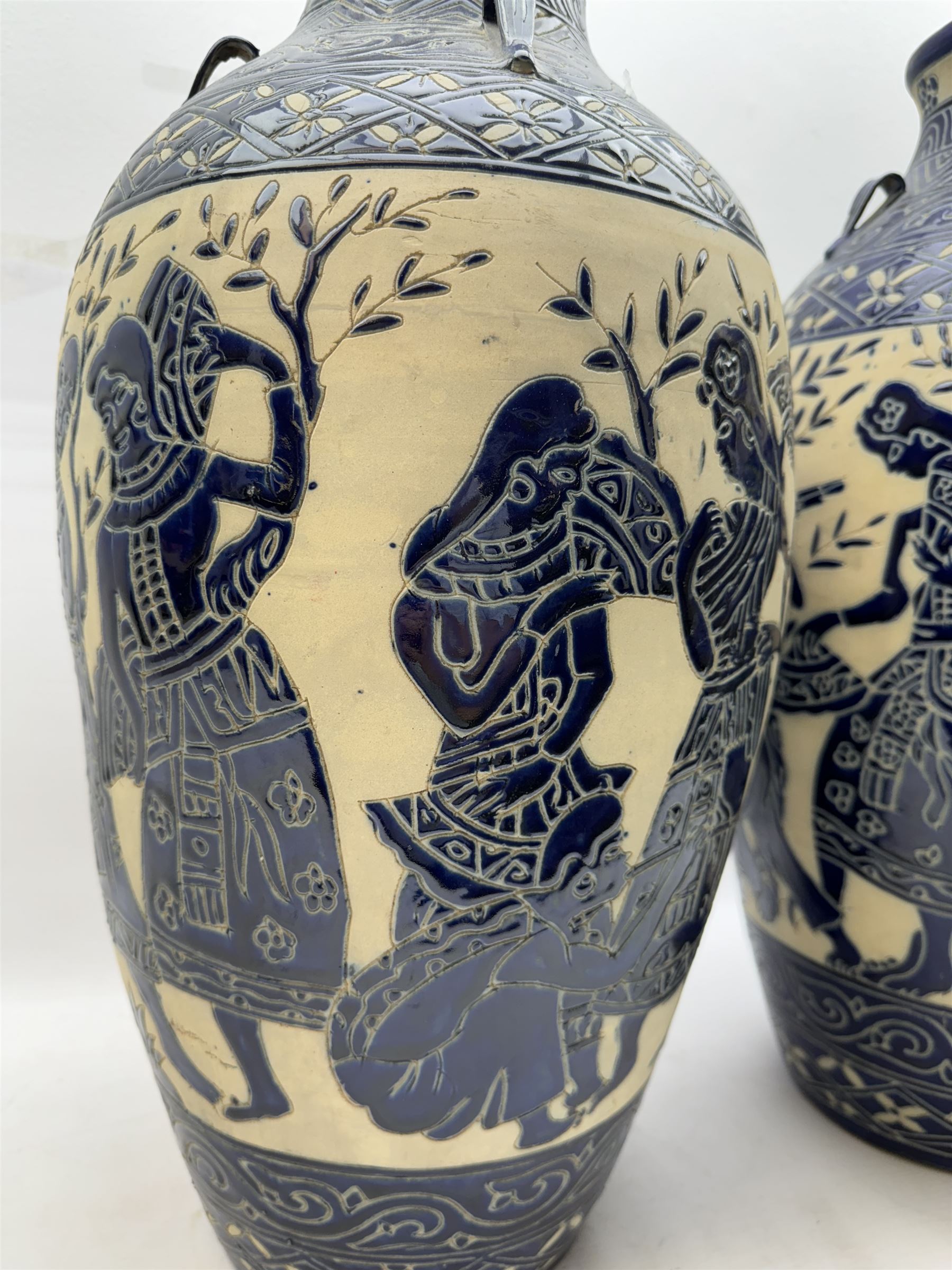 Pair of blue and white Cretan style vases, decorated with figures among trees with blue boarders on a white ground, H55cm