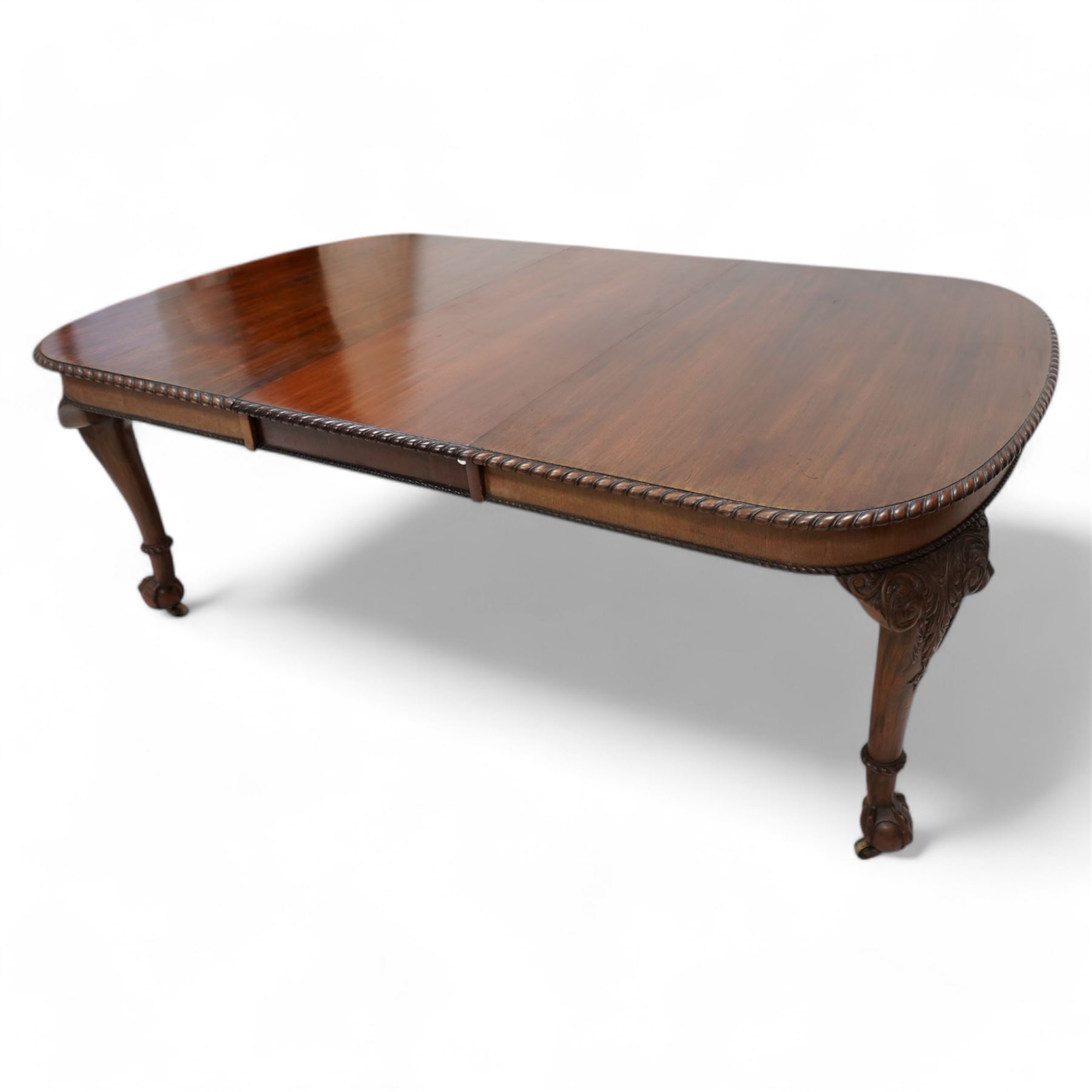 Early 20th century telescopic extending dining table, gardroon carved rectangular top with rounded ends, scrolled acanthus leaf carved cabriole supports with ball and claw feet, on brass castors, with two additional leaves  