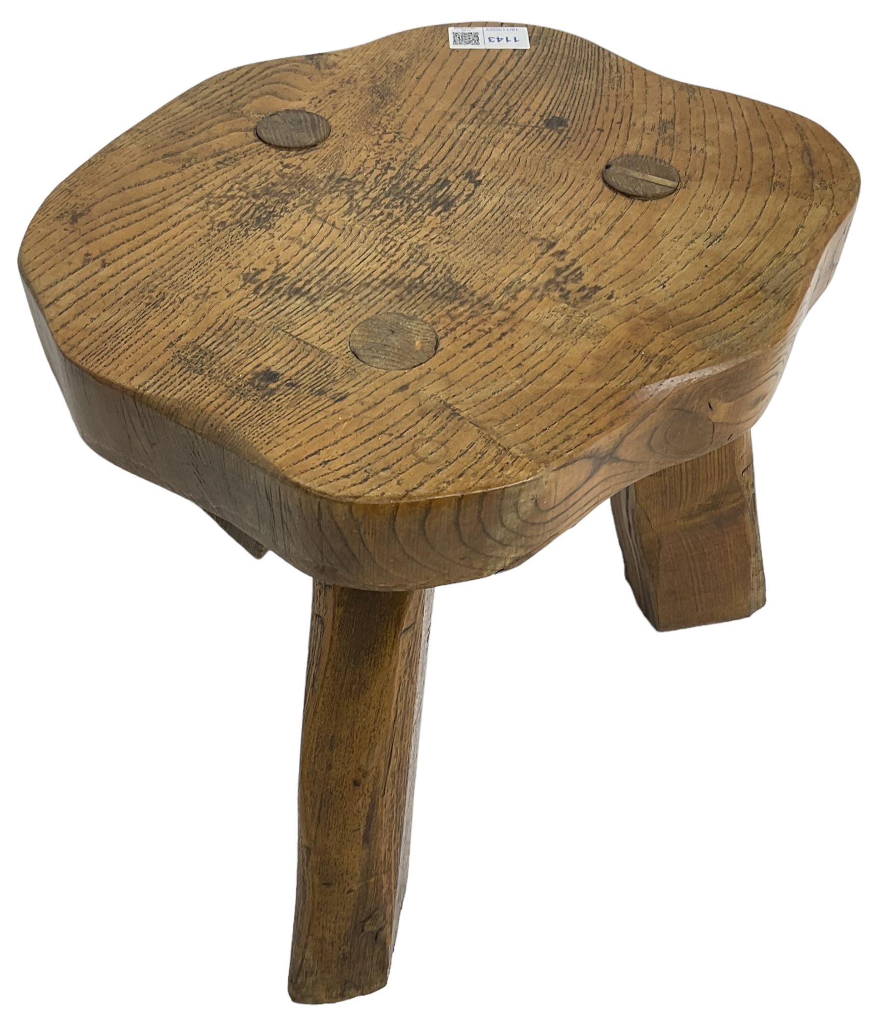 Small rustic elm three-legged stool, with metal plaque to the underneath inscribed 'Wandewood' 