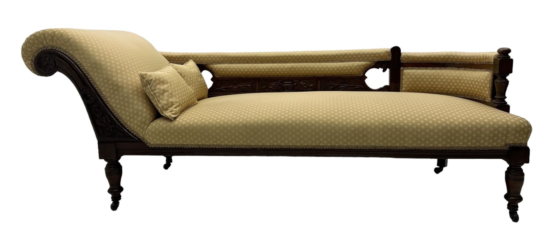 Late Victorian walnut framed chaise longue, scrolled backrest and sides upholstered in patterned yellow fabric, carved floral motifs to the backrest and sides, raised on turned supports with castors