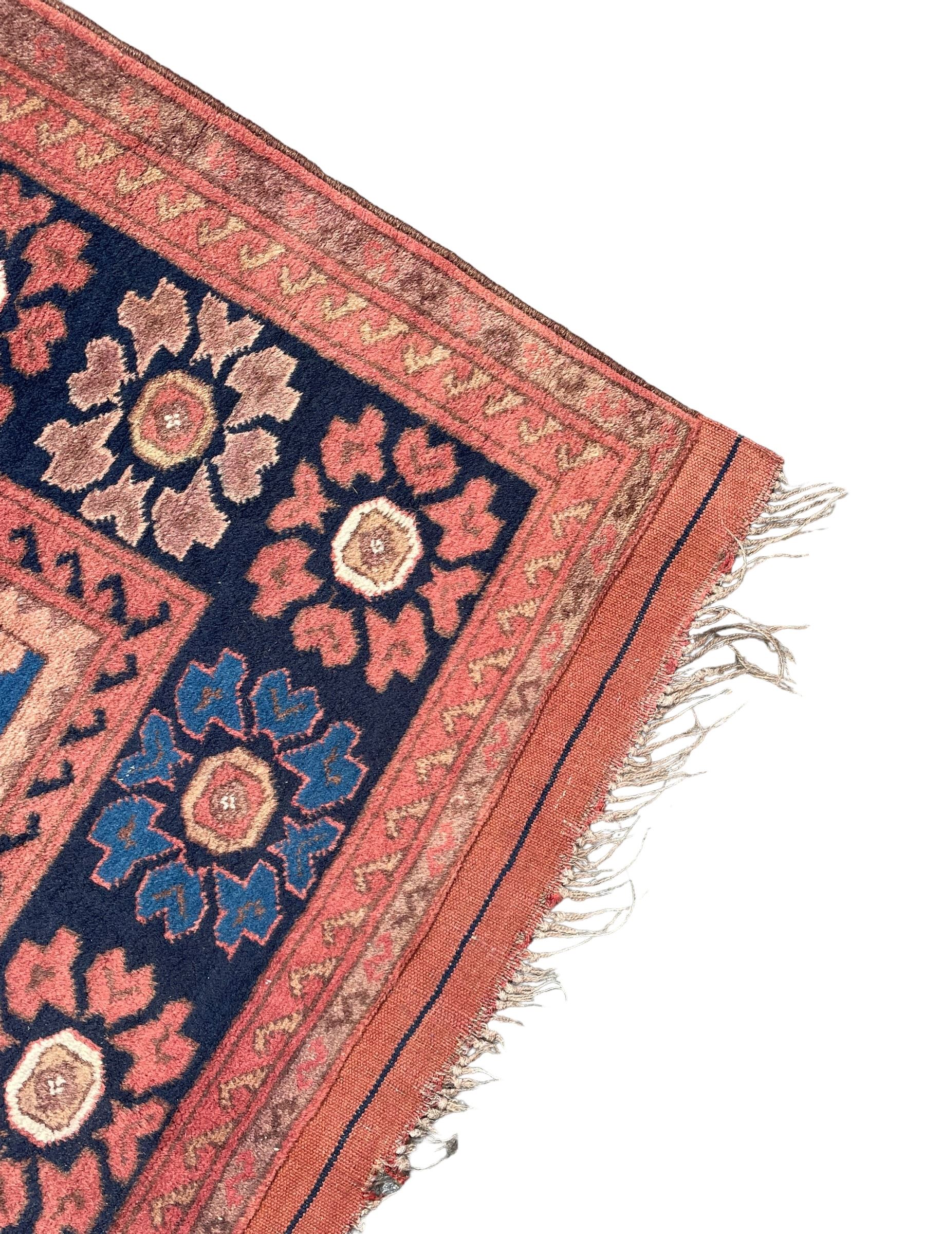 Afghan rust ground carpet, large central lozenge medallion decorated with stylised plant motifs, running water guard stripes enclosing indigo ground border decorated with stylised flower heads