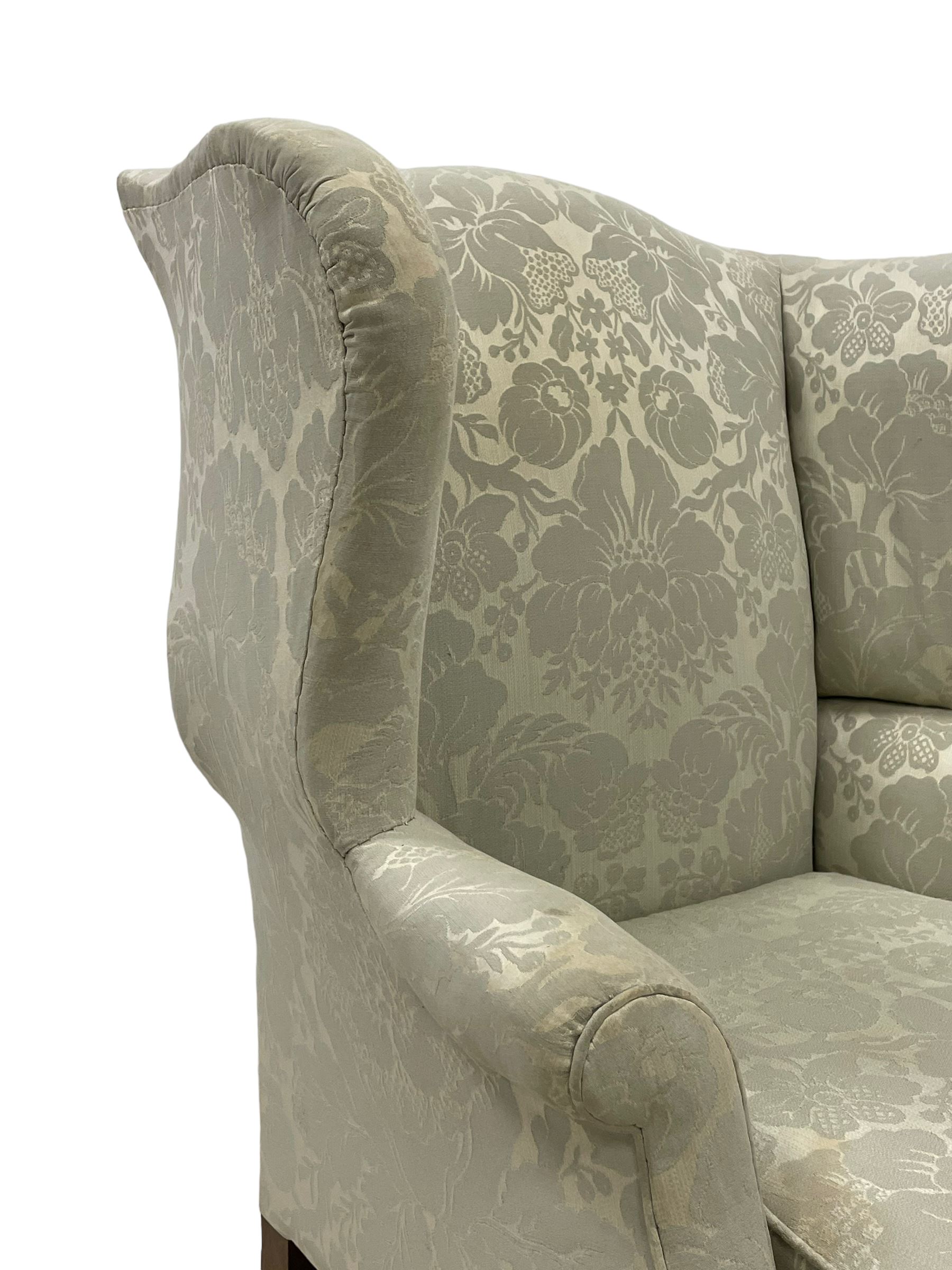 Georgian mahogany framed wingback armchair, upholstered in floral pattern silk damask fabric, wide seat enclosed by rolled arms, on chamfered square supports united by plain stretchers 