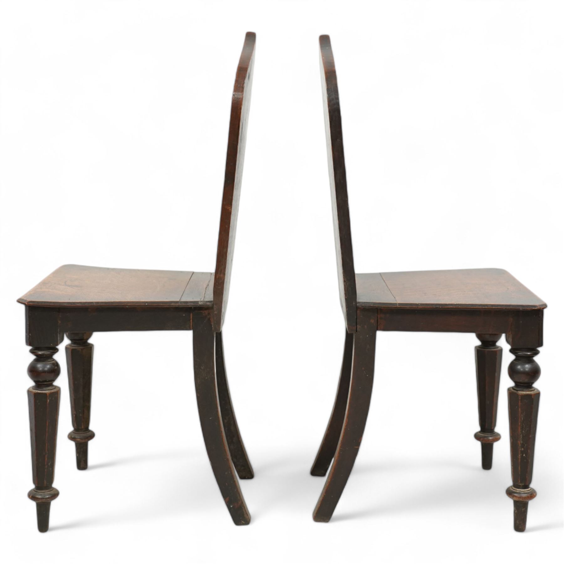 Pair of 19th century carved oak hall chairs, the arched back carved with moulded scalloped decoration with a central applied shield motif, canted panelled seat over turned octagonal supports