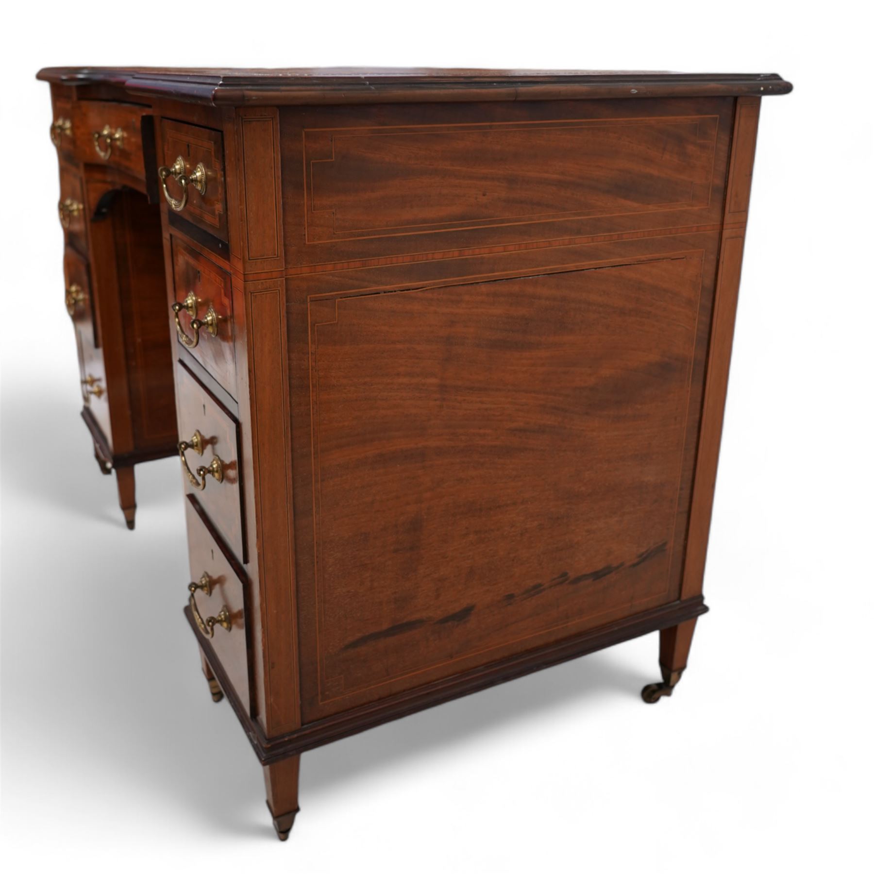 Edwardian inlaid mahogany reverse break bowfront desk, moulded satinwood banded top with inset leather writing surface, fitted with nine drawers, on square tapering feet with brass cups and castors 