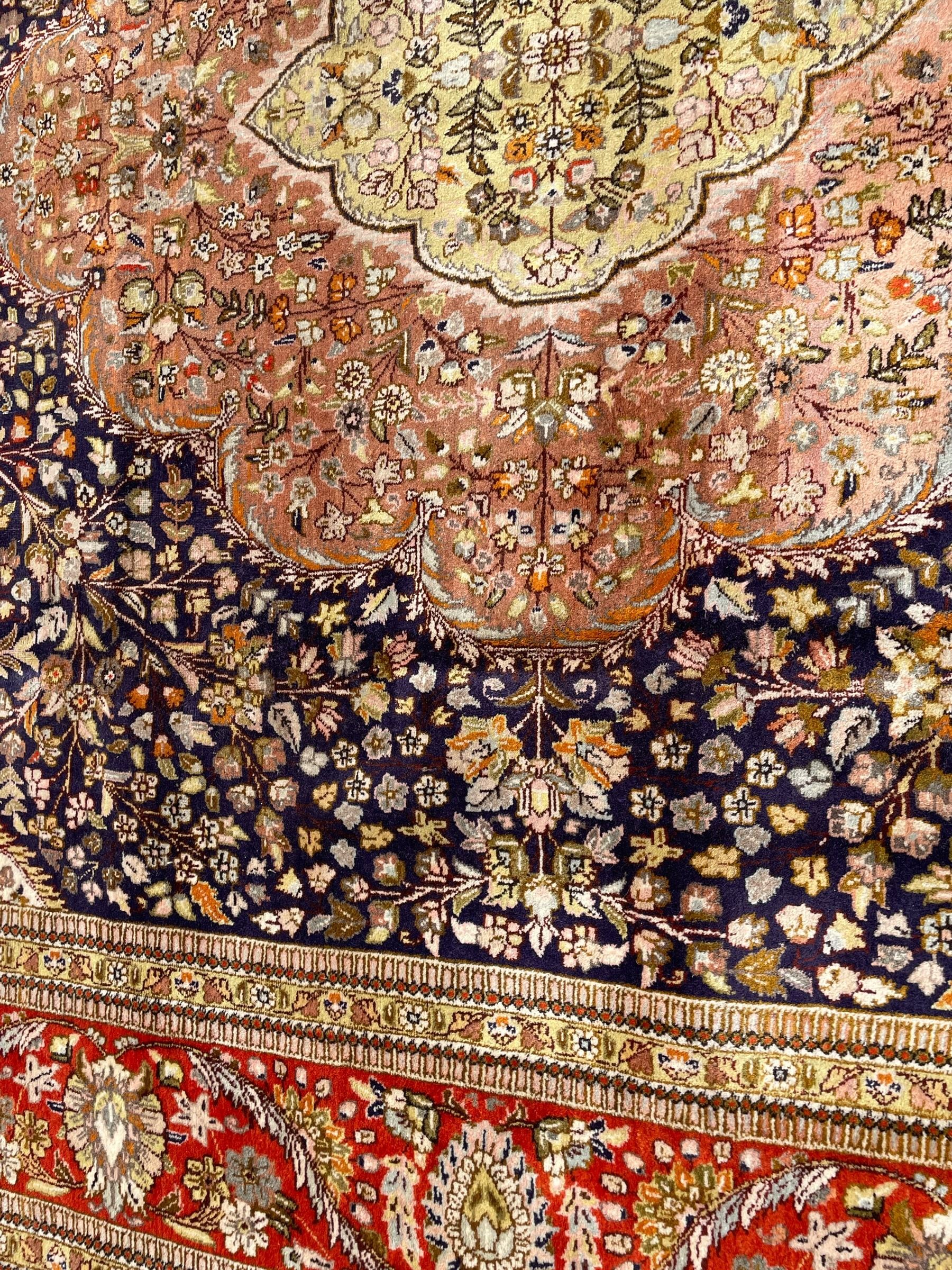 Persian Kashan, scalloped central medallion on indigo ground field, decorated profusely with branch shoots with floral motifs, pale ground spandrels decorated with stylised flower head motifs, crimson ground border decorated with repeating palmettes and trailing leafy branches, within multiple guard stripes 