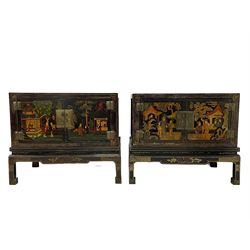 Pair of early 20th century Chinese ebonised and lacquered wood cabinets, the top decorated with dragons over lapping waves within a gilt patterned panel, the surrounding band decorated with Chinese symbols and flowerheads, enclosed by two doors each with village scenes with pagodas, figures and trees, the panelled sides decorated with a figure riding a dragon on stands with gilt decorated 