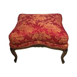 Late 20th century French design stained beech framed armchair and matching stool - the armchair with shaped and moulded frame carved with flower heads and foliage, upholstered in silk red and gold ground fabric with floral pattern, on scroll carved cabriole feet decorated with flower head carvings (W73cm, H82cm, D75cm); the footstool of concaved rectangular form with moulded frame carved with flower heads, upholstered loose cushion, on cabriole feet (70cm x 64cm, H48cm)