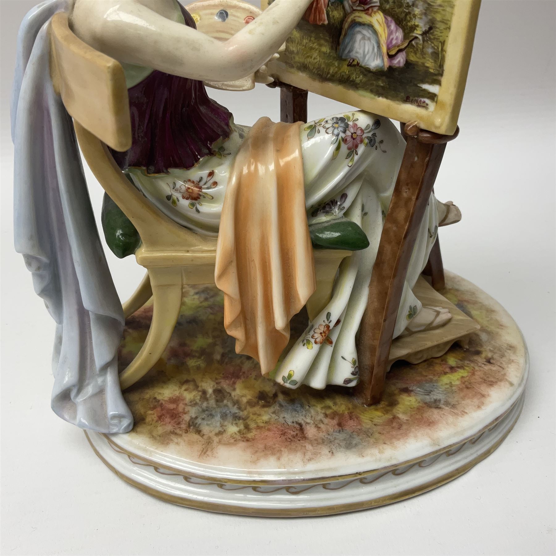 Pair of late 19th/early 20th century Naples figures modelled engaged in the arts, the first example modelled as a female figure seated before an easel, painting a figural scene, the second modelled as a female figure seated before a bust with scultping tools in hand, each upon an oval base with naturalistic painted ground, each with blue crowned N mark beneath, each approximately H16cm, including base L15xm
