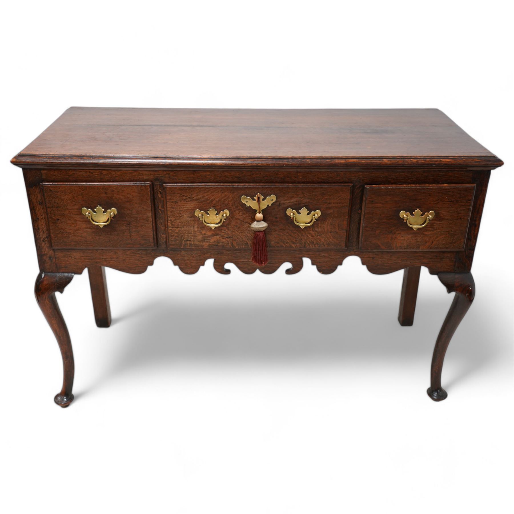 18th century oak dresser base, the rectangular top with moulded edge, fitted with three drawers with original brass handle plates, over a shaped frieze, raised on front cabriole supports with pad feet