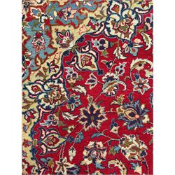 Persian Kashan red ground rug, the field decorated with a central floral medallion surrounded buy scrolling vine motifs and palmettes, the main border featuring a series of stylised floral motifs against a dark blue ground, enclosed by multiple guard stripes with alternating floral and geometric designs