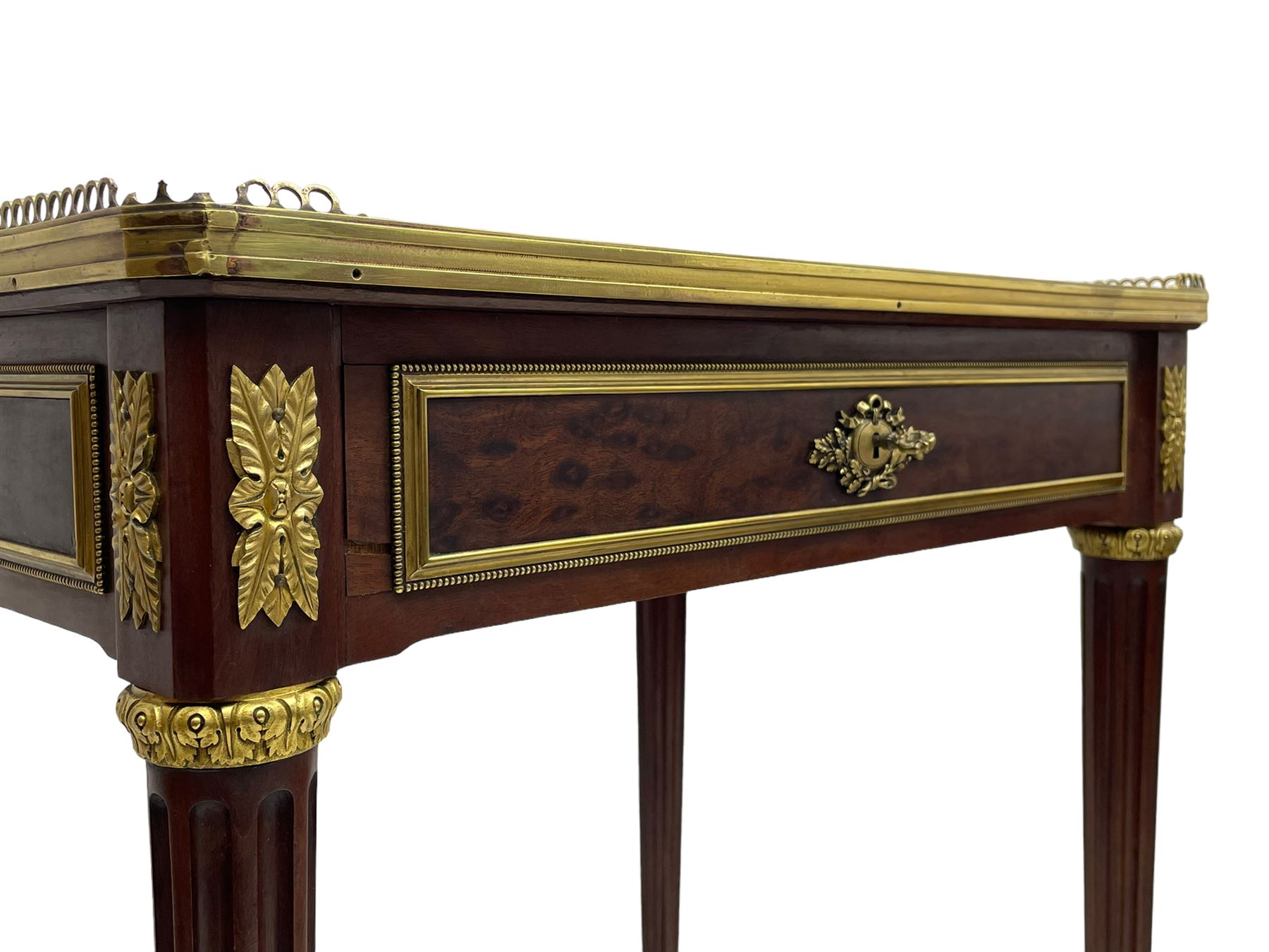 Late 19th century French figured plum pudding mahogany side table, canted rectangular white marble top with raised gilt metal gallery, fitted with a single frieze drawer, central extending floral cast ormolu escutcheon and applied moulded edging, on tapering turned and fluted supports with brass cups and castors, decorated with cast foliate mounts and foliate cast collars 