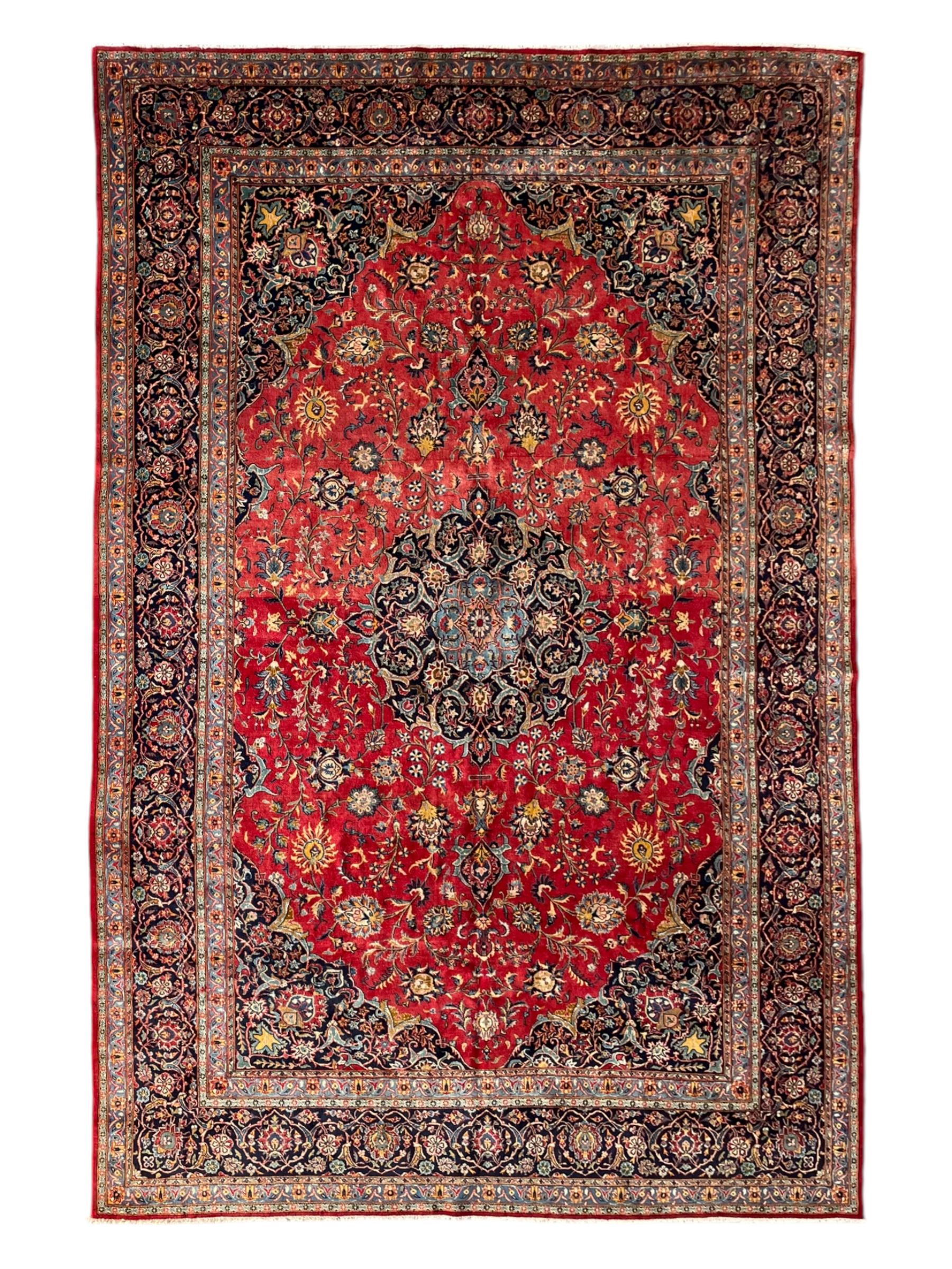 Persian Kashan crimson ground carpet, central rosette medallion on a field of trailing foliate branches decorated with palmettes, scrolling border with repeating plant motifs and flower heads, enclosed within floral pattern guard stripes