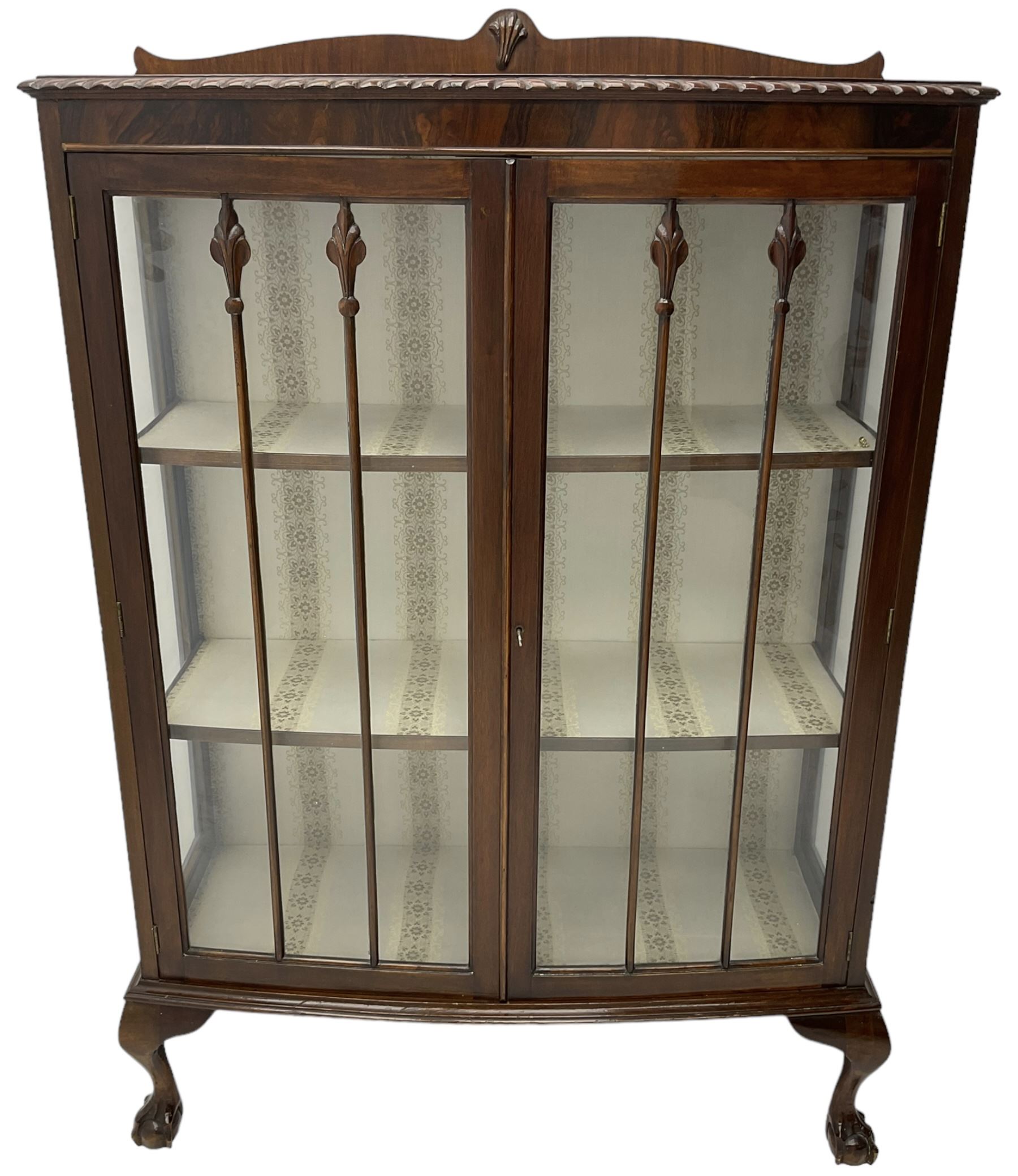 Early 20th century figured walnut bow-front display cabinet, enclosed by two glazed doors, on ball and claw cabriole feet