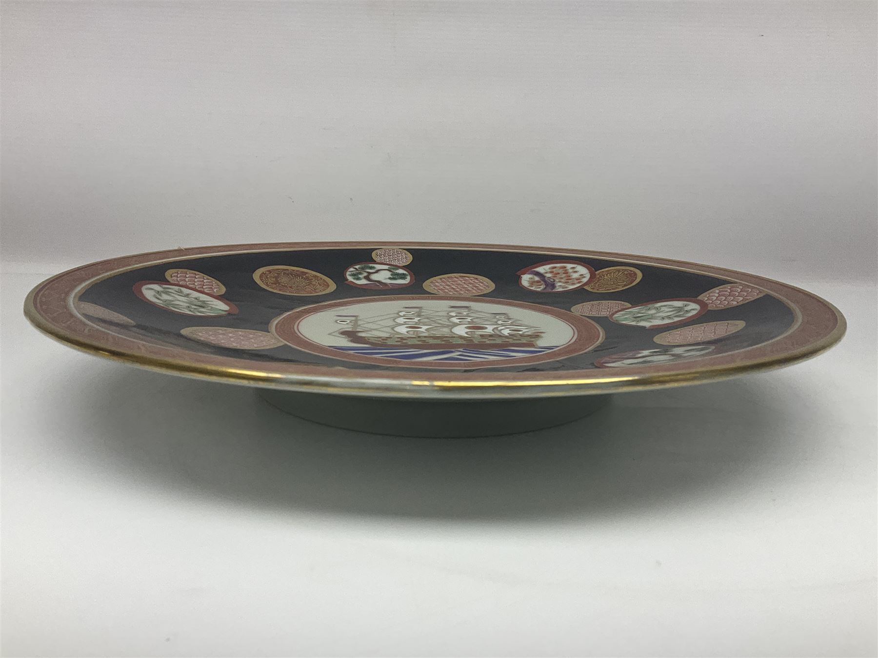 Chinese export charger, the centre decorated in enamel with a ship at full sail, surrounded by enamel panels of bamboo and cherry blossom with gilt edging on a black ground, with red and gilt border, with painted character marks beneath D34.4cm