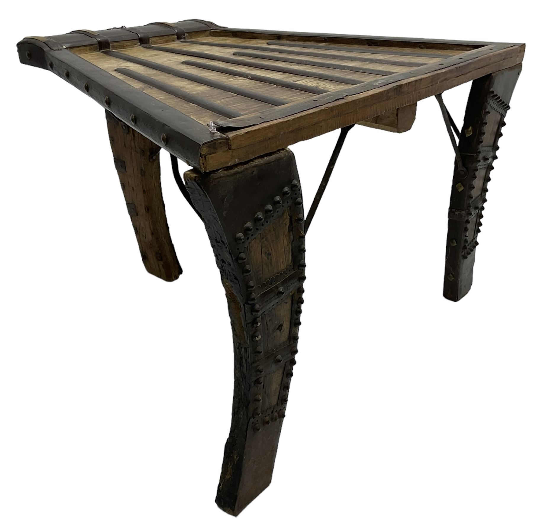 19th century Indian bullock / ox cart converted coffee table, trapezoidal top with applied metal decoration and iron stretchers, raised on three swept supports with stud decoration