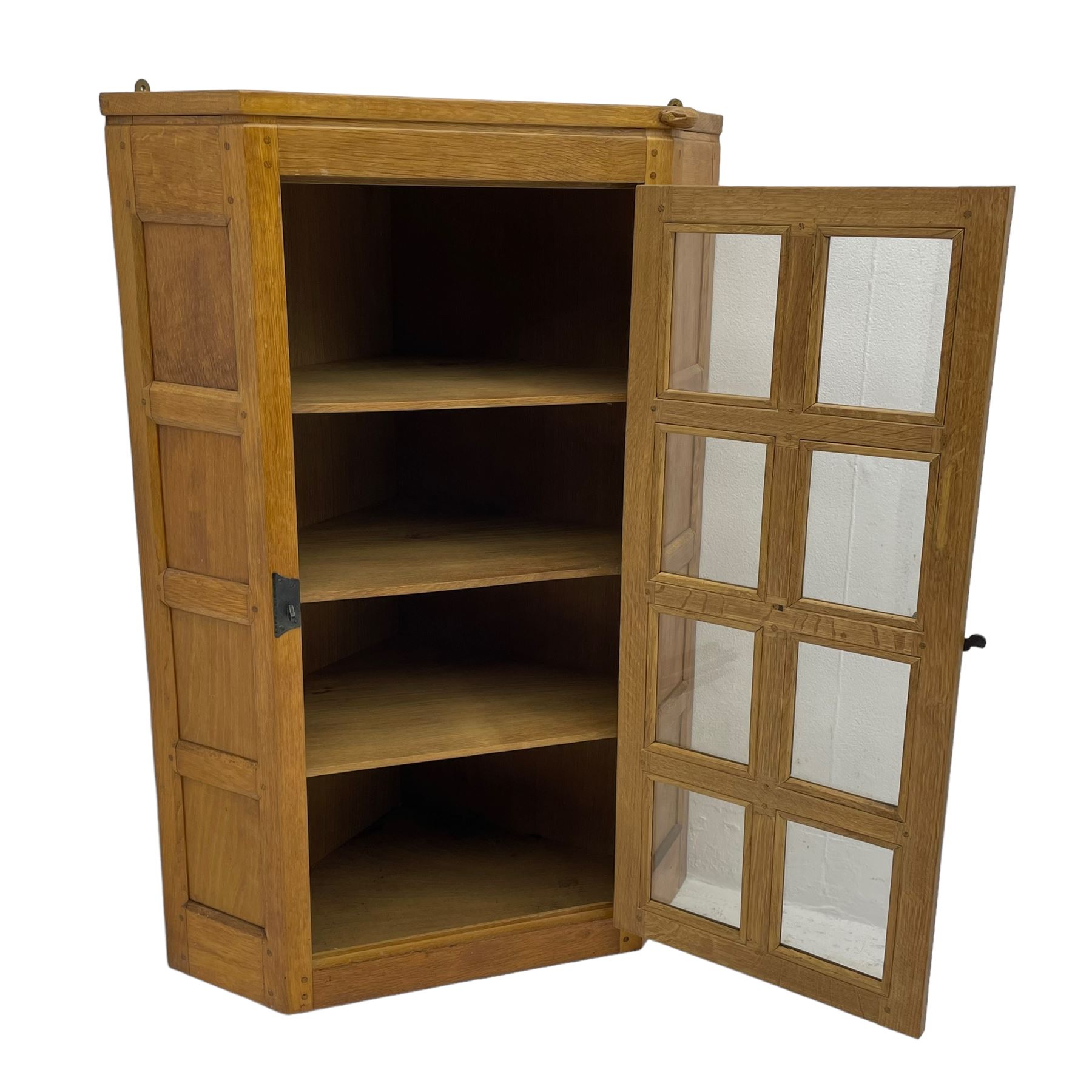 Rabbitman - oak corner cabinet, astragal glazed door enclosing three internal shelves, panelled upright corners, fitted with wrought metal hinges and latch, carved with rabbit signature, by Peter Heap, Wetwang 