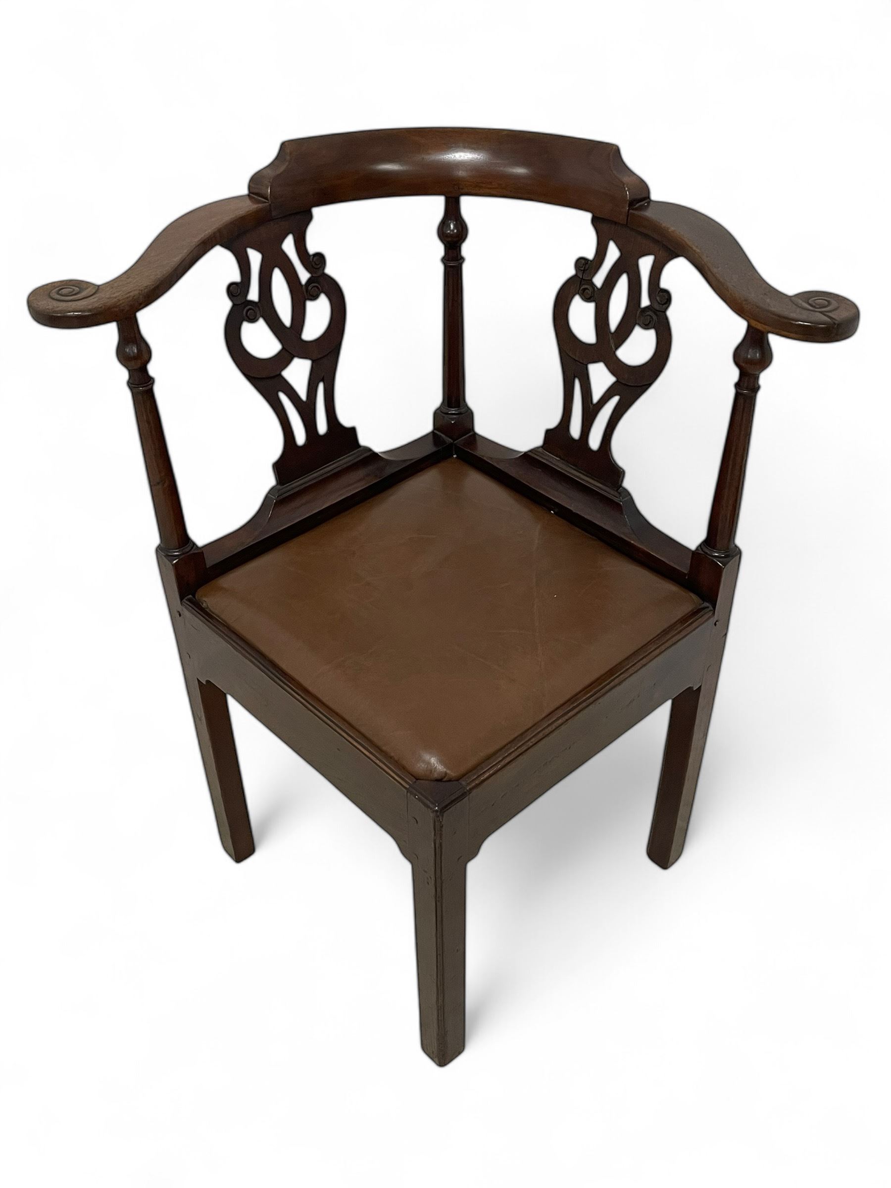 George III mahogany corner elbow chair, curved back rest and shaped arms with scroll carved terminals, on turned supports and pierced scroll carved interlaced splats, drop-in seat upholstered in brown leather, on square supports with inner chamfer and outer moulding 