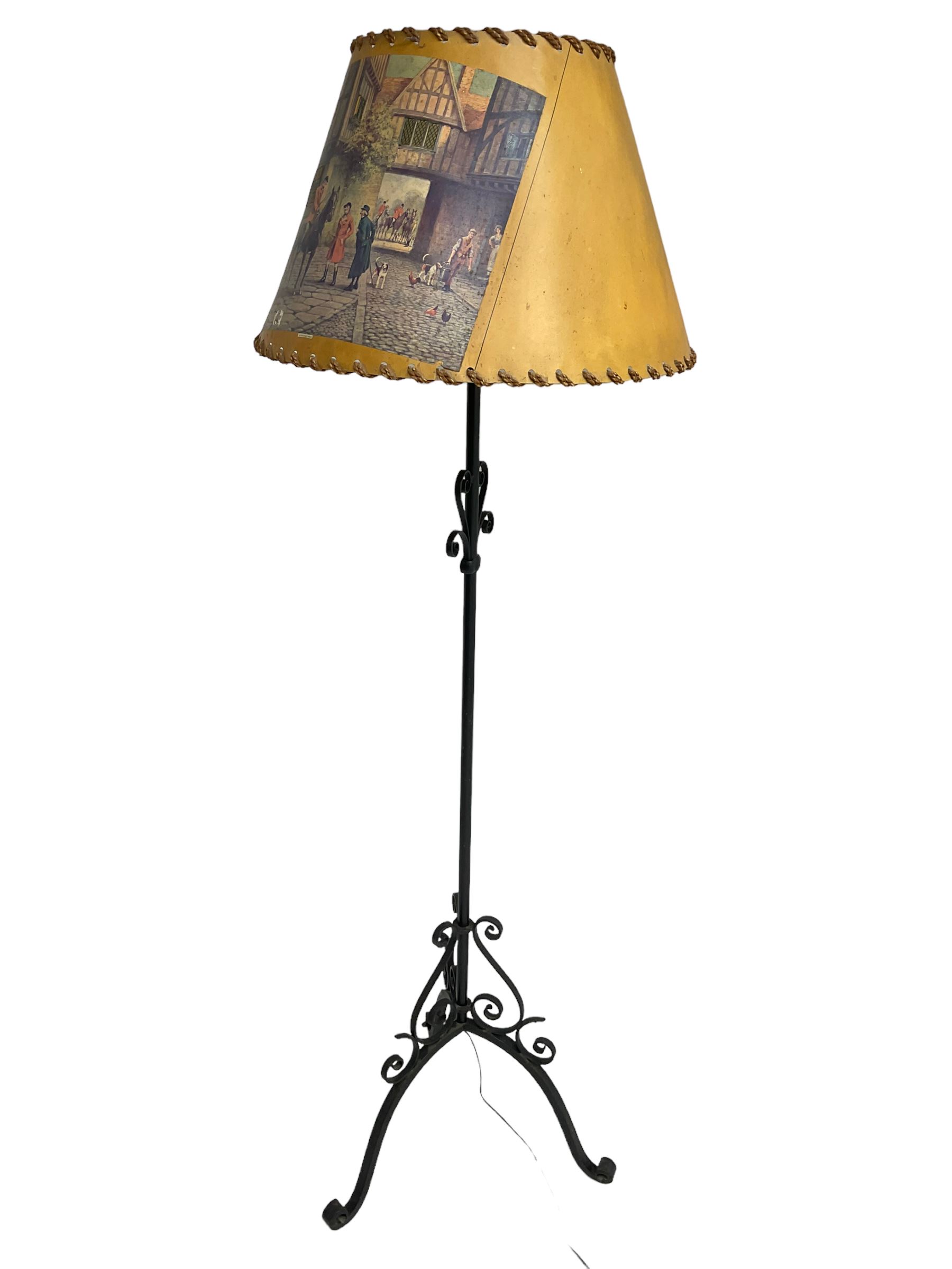 20th century wrought metal standard lamp, decorated with scrolls and on tripod base, with conical shade depicting hunting scene (H172cm); and a wrought metal wall hanging flower pot holder (W92cm)