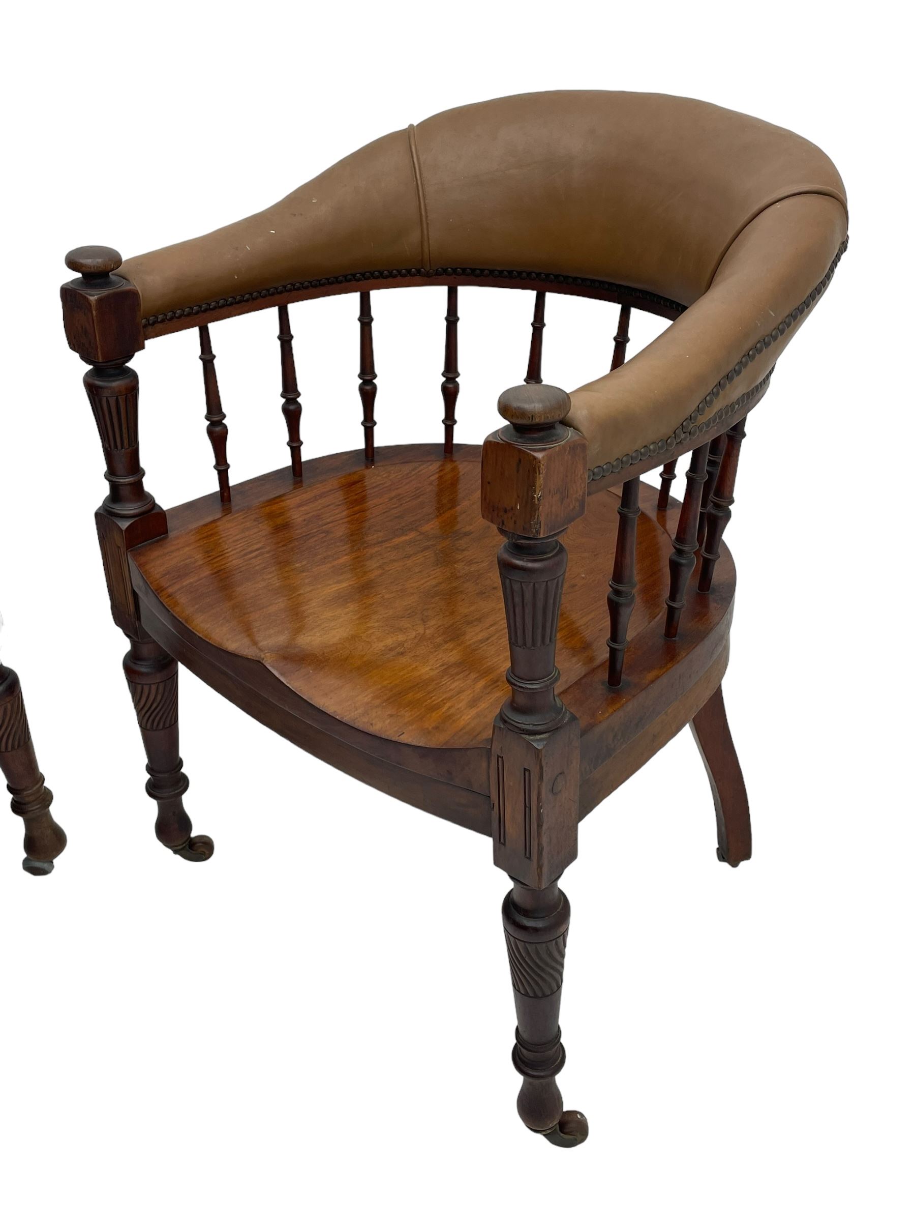 Pair of late Victorian walnut tub-shaped elbow chairs, the cushioned cresting rail upholstered in leather on spindle turned supports, dished saddle seat on turned supports