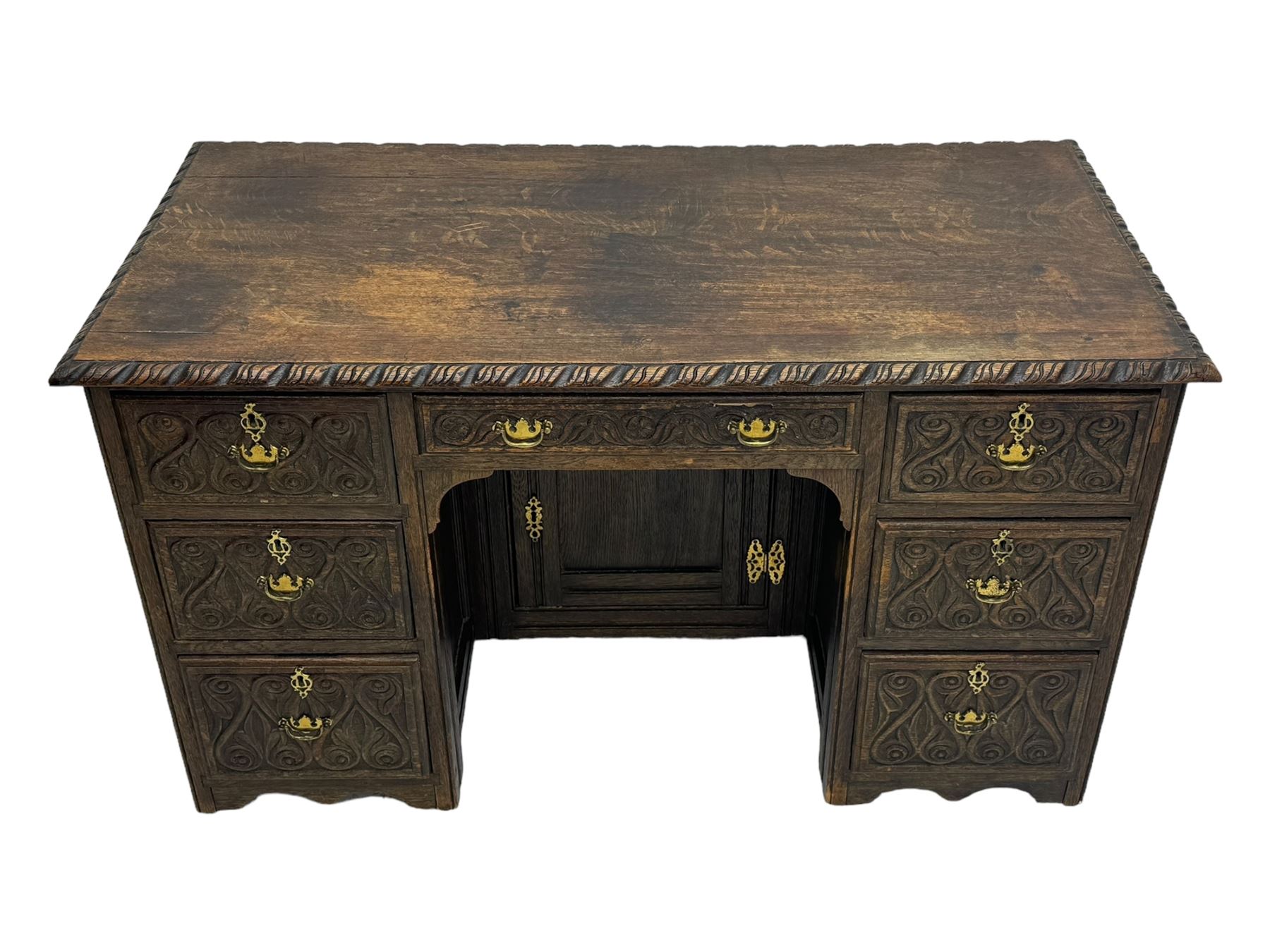 Victorian carved oak kneehole desk, the rectangular top with carved edge, above central drawer with carved front and brass handles, central kneehole with cupboard door, flanked by two banks of three graduating drawers each with similarly carved decoration, on shaped plinth base with castors