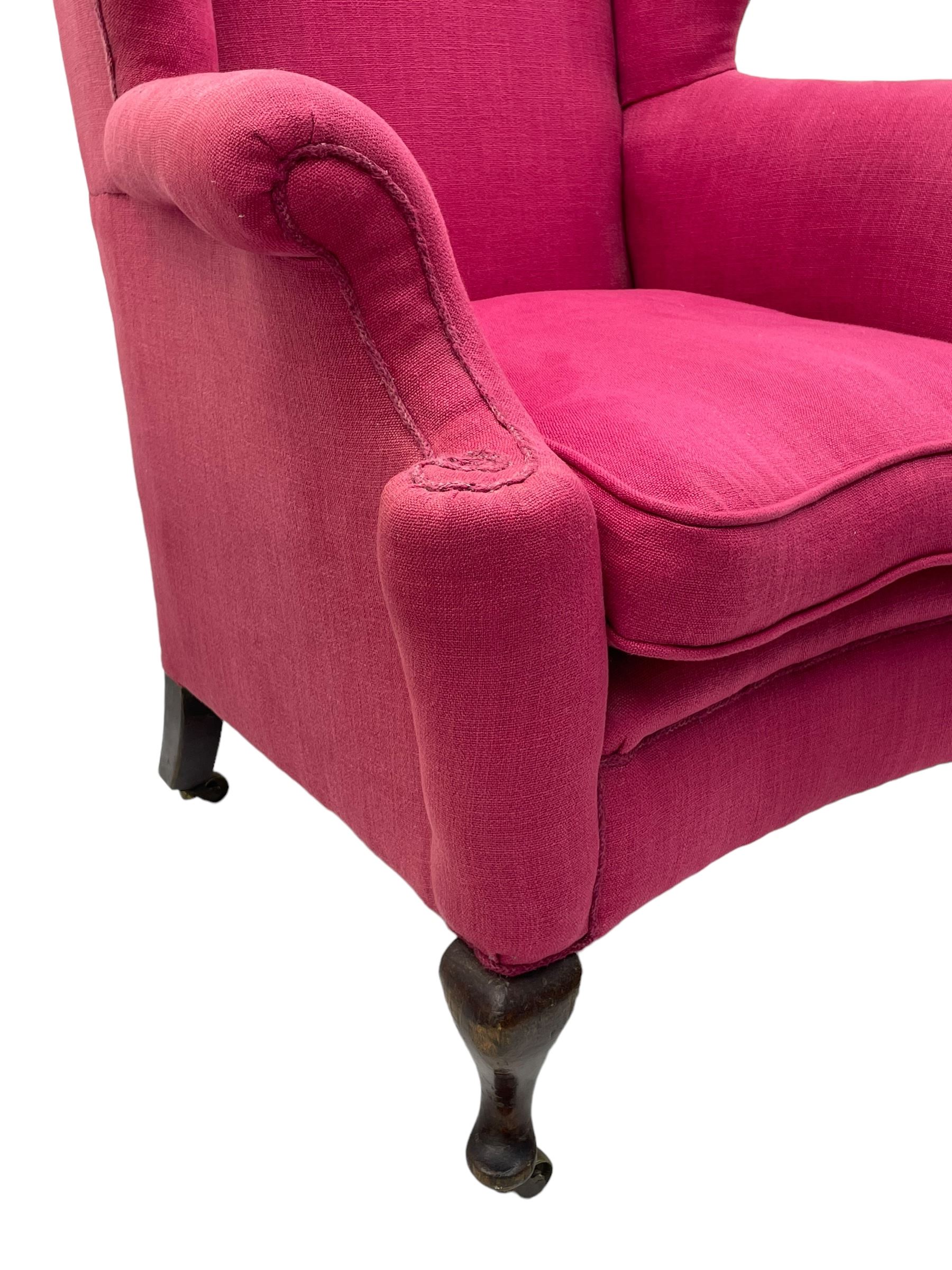 Georgian design hardwood-framed wingback armchair, arched cresting rail over curved wingback, rolled arms on scrolled cushioned supports, reverse bow-front, upholstered in claret red fabric with loose seat cushion, on cabriole front feet and brass castors 