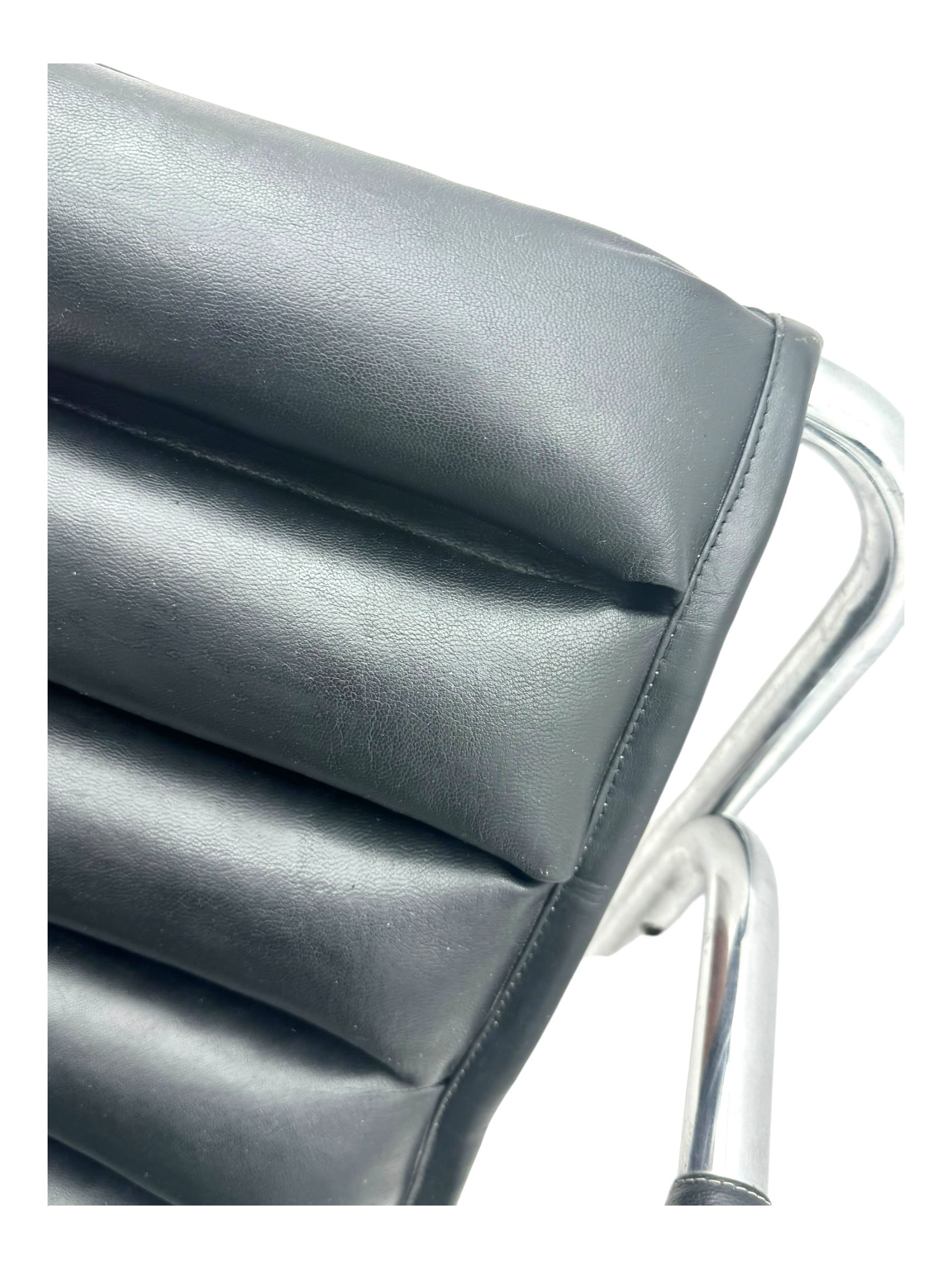 Baroumand Designs - pair of mid 20th century modernist armchairs, slung black leather seat with horizontal channel tufting, tubular chrome frame with curved arms, raised on tubular supports