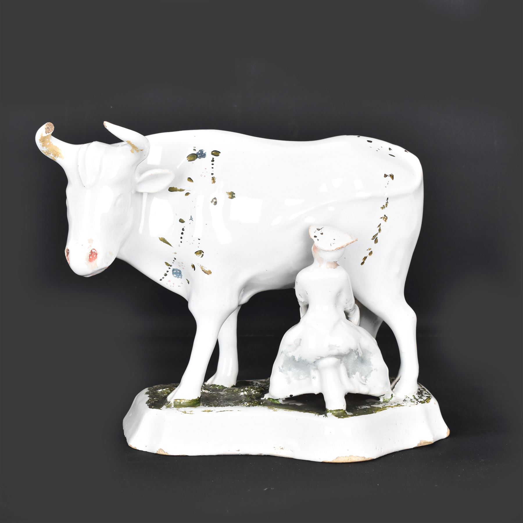 19th century Delft figure group depicting a milkmaid milking a cow, H17.7cm