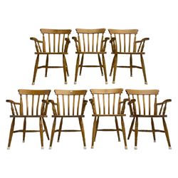 Set of seven beech farmhouse dining elbow chairs, stick back over saddle sat, raised on ring turned supports united by H-stretcher