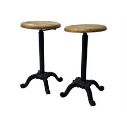 Pair of 20th century machinist stools, each with height-adjustable beechwood circular seats, supported by cast iron pedestal bases with four splayed feet