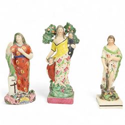 Three early 19th century Staffordshire Pearlware figures depicting Faith, Hope and Charity, Faith standing next to a shield bearing a cross, on an oval encrusted and moulded base H20cm, Charity stood holding a child and another by her side and Hope standing with an anchor, both on square bases (3)