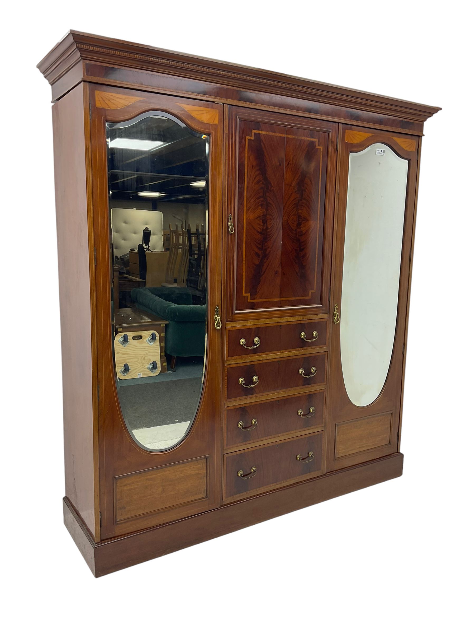 Edwardian inlaid mahogany combination wardrobe, projecting moulded cornice over figured frieze with satinwood banding, the central section fitted with cupboard over four long drawers, figured matched veneers and satinwood bands, flanked by two full height compartments enclosed by bevelled shield shaped mirror doors, satinwood fan inlaid spandrels, on moulded skirt base 